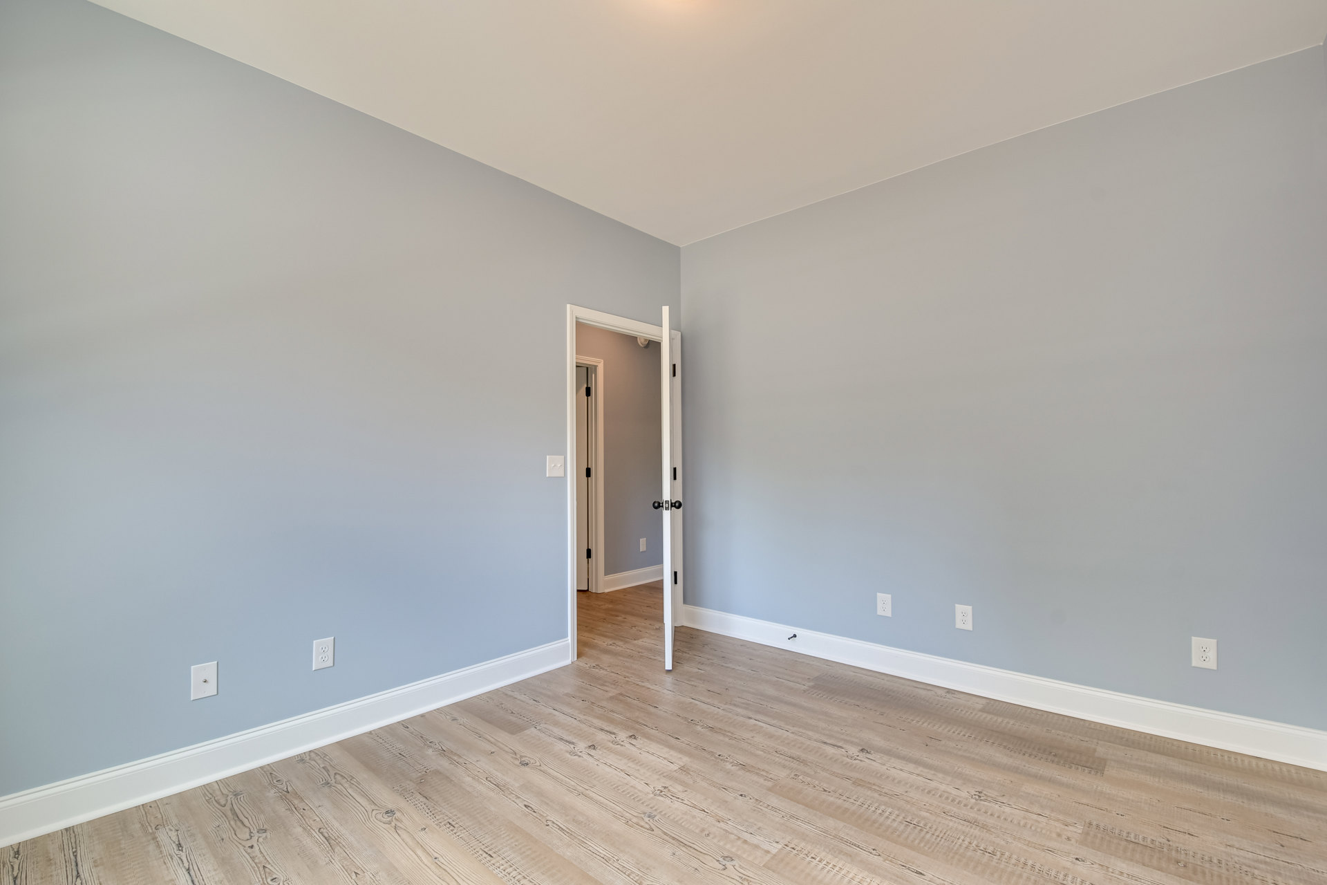 Wood floor with white table against a blue wall, open door with black handle, white ceiling featuring recessed light