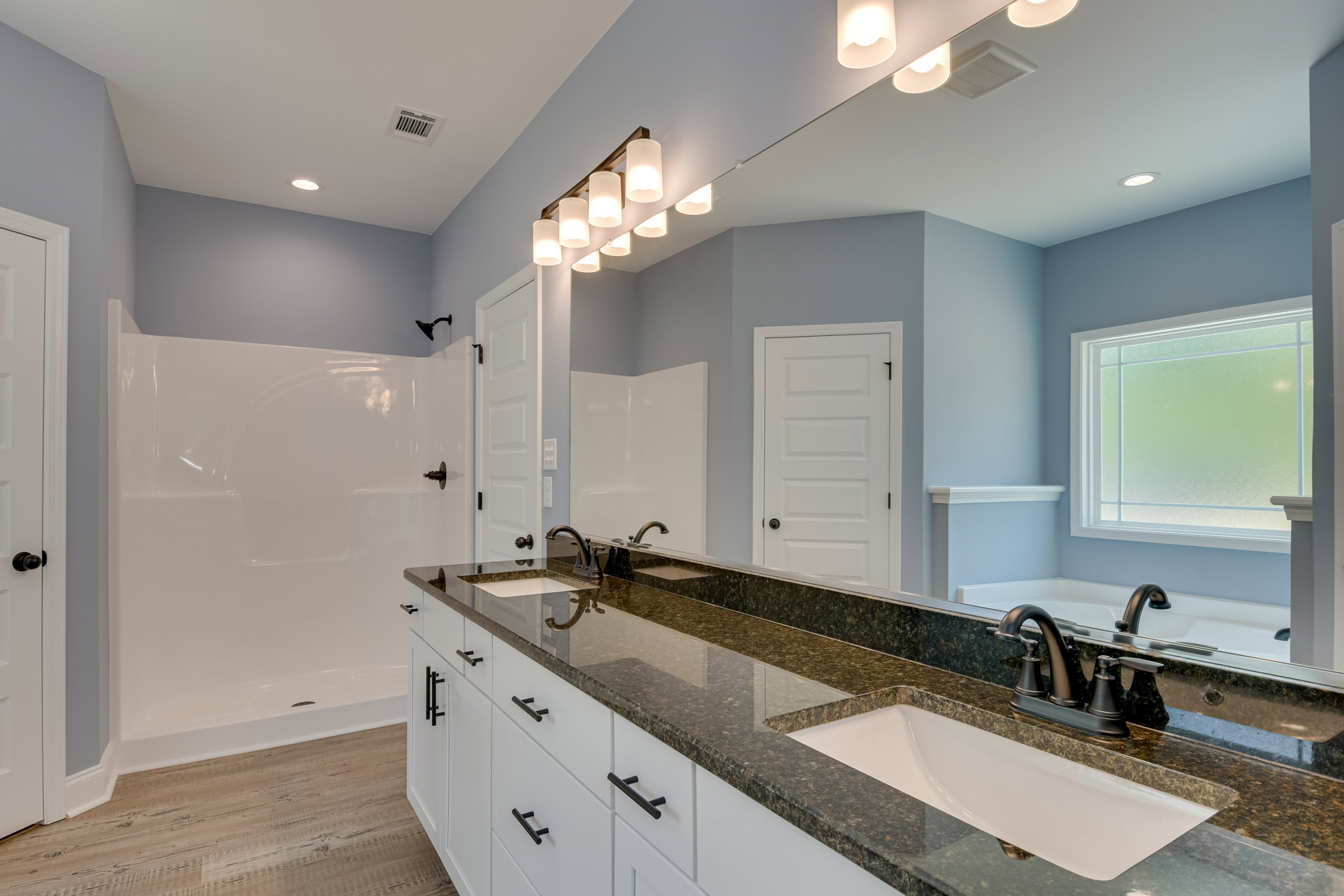 Bathroom with marble countertop, wide rectangular sink, expansive mirror, frosted glass window, white cabinetry with black handles, recessed lighting in ceiling