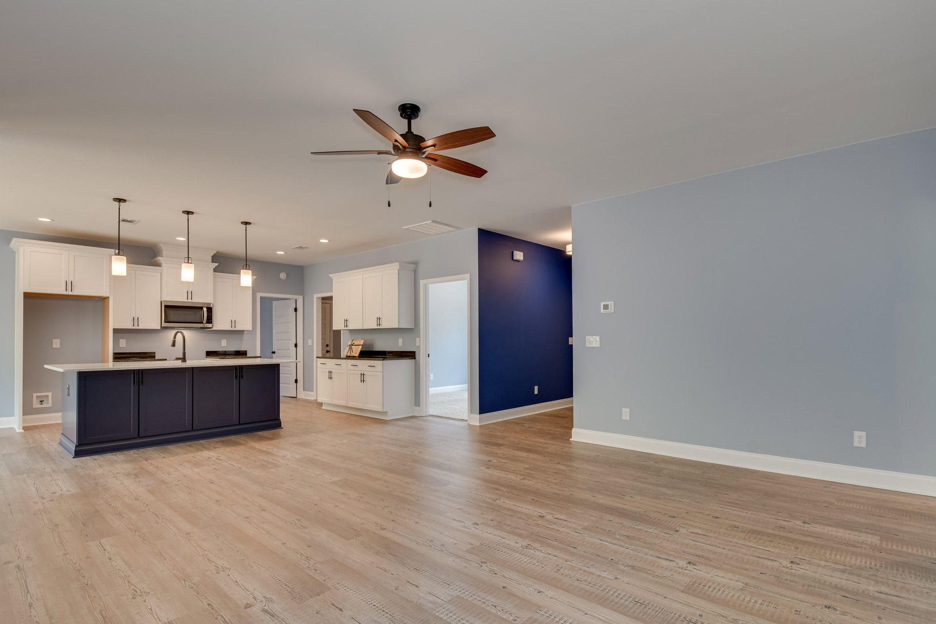 Open concept kitchen and living area with hardwood floors, ceiling fan with light, white cabinetry, kitchen counter with sink, and white door with matching frame.