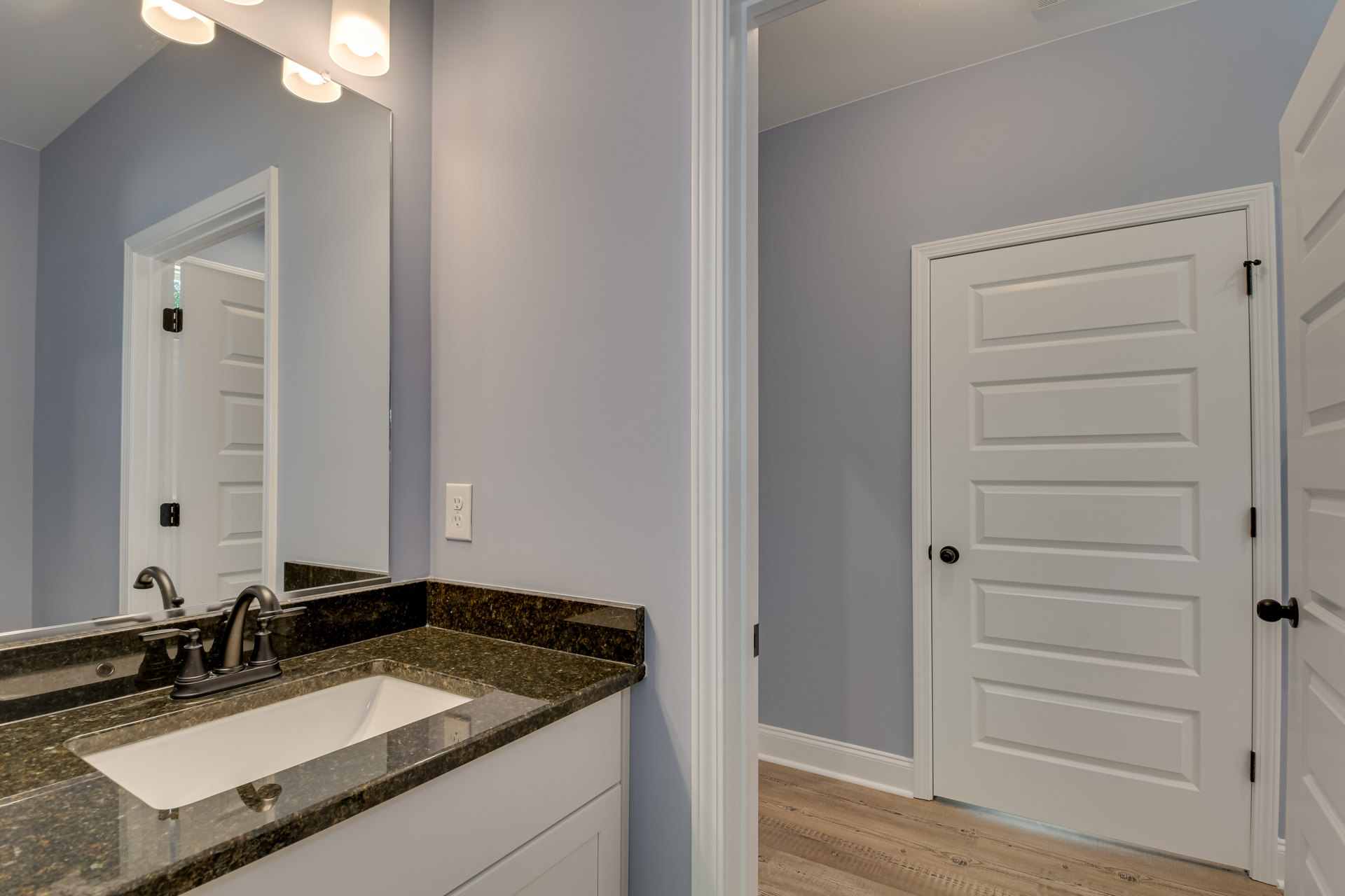 Marble countertop with black faucet and undermount sink, large mirror above, white door with black knobs, light-colored tile walls and cabinetry