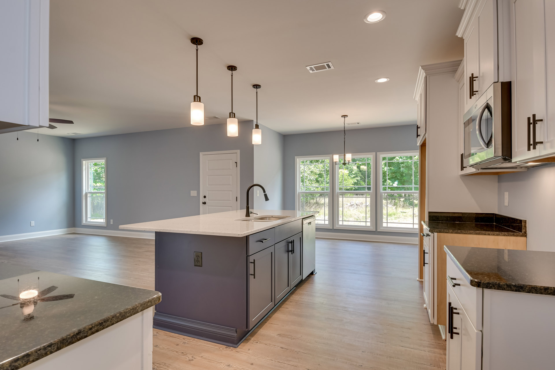 Kitchen with marble island featuring built-in sink and chrome faucet, pendant lights above, white cabinetry, three windows, and white door with black handle.