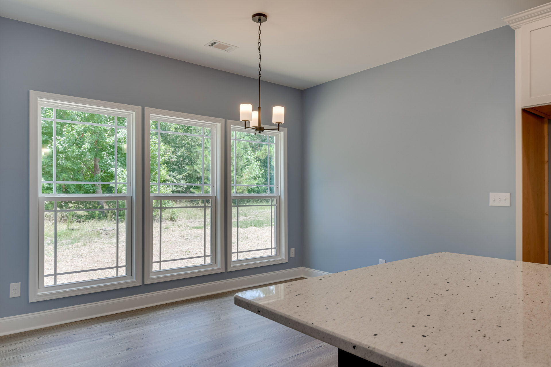 Marble table centered in a bright room with large windows overlooking trees, laminate flooring, and a ceiling chain fixture.