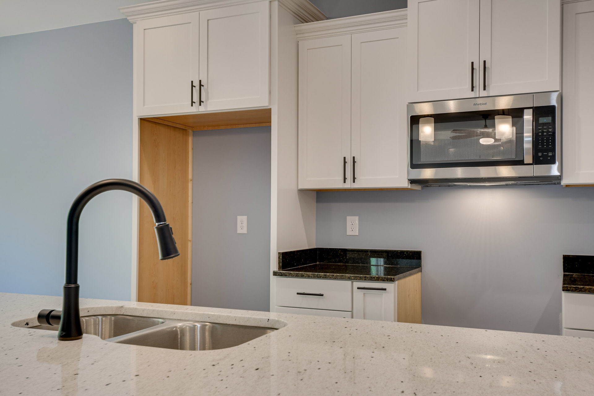 White kitchen cabinets, black faucet on a light countertop, built-in microwave, stainless steel sink, white bowl, modern appliances