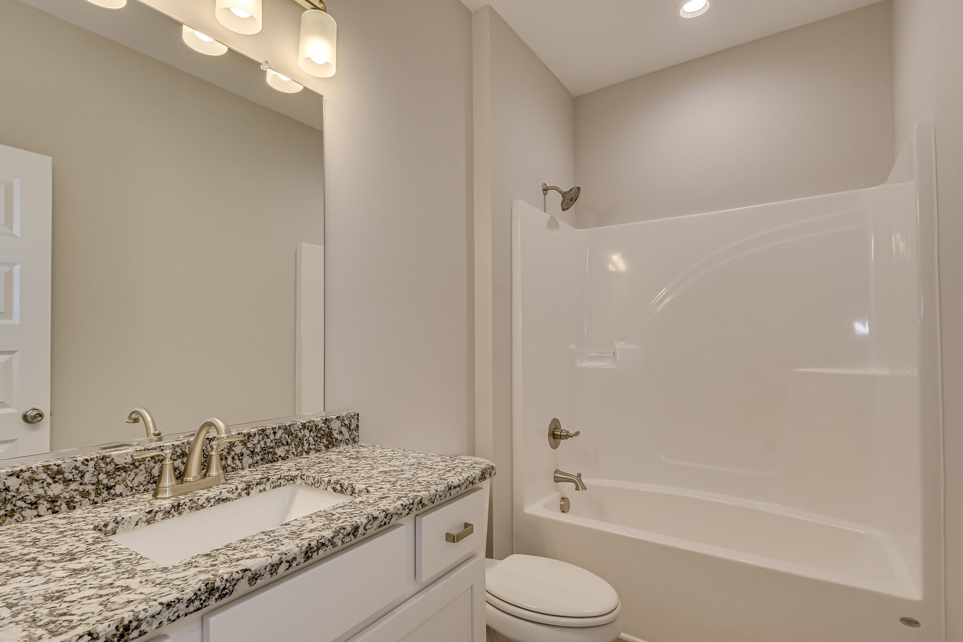 Modern bathroom featuring a white bathtub, tiled shower with chrome showerhead, white toilet with closed lid, and a sink with a sleek faucet set on a stone countertop; overhead