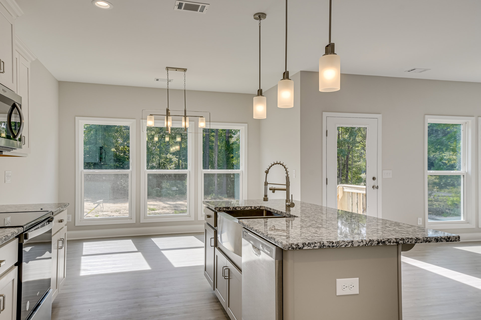 Marble kitchen island with built-in sink, white cabinetry, stainless steel appliances, pendant light fixture overhead, large window with tree views