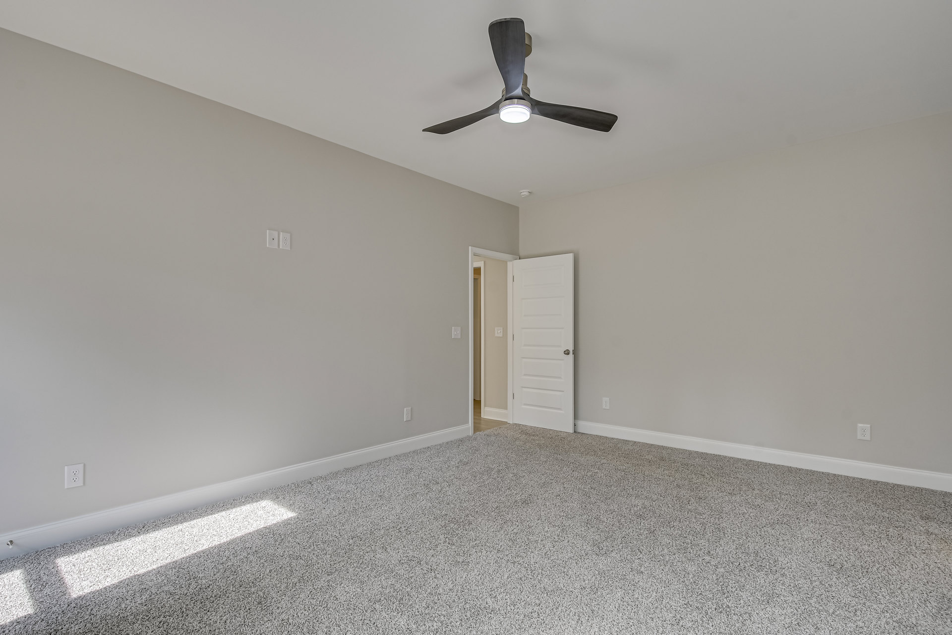 Neutral-toned room with white carpet, ceiling fan with light fixture, white door with silver doorknob, light switch on wall, plaster walls and ceiling