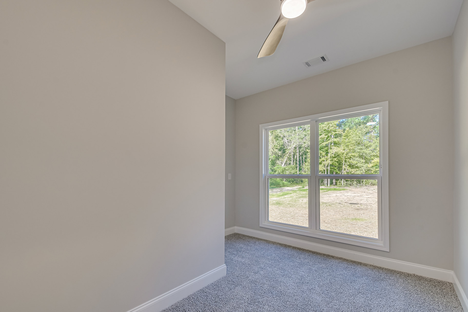 Bright room with white plaster walls, large window overlooking trees, ceiling fan with light fixture, wood flooring, and crown molding.