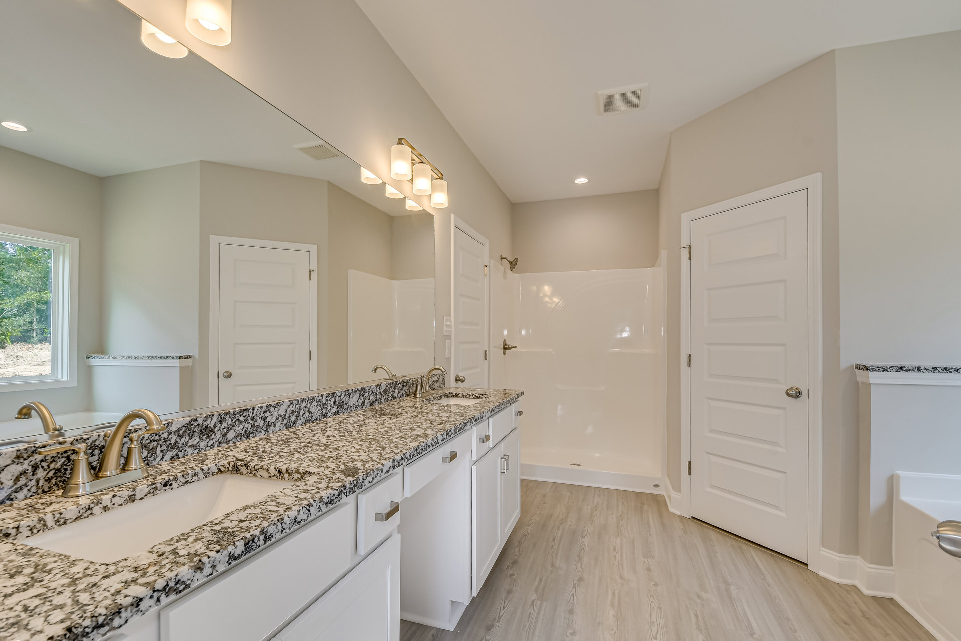 Bathroom with marble countertops, glass-enclosed shower, white cabinetry, silver and gold door handles, window overlooking trees, modern sink and faucet, close-up of contemporary