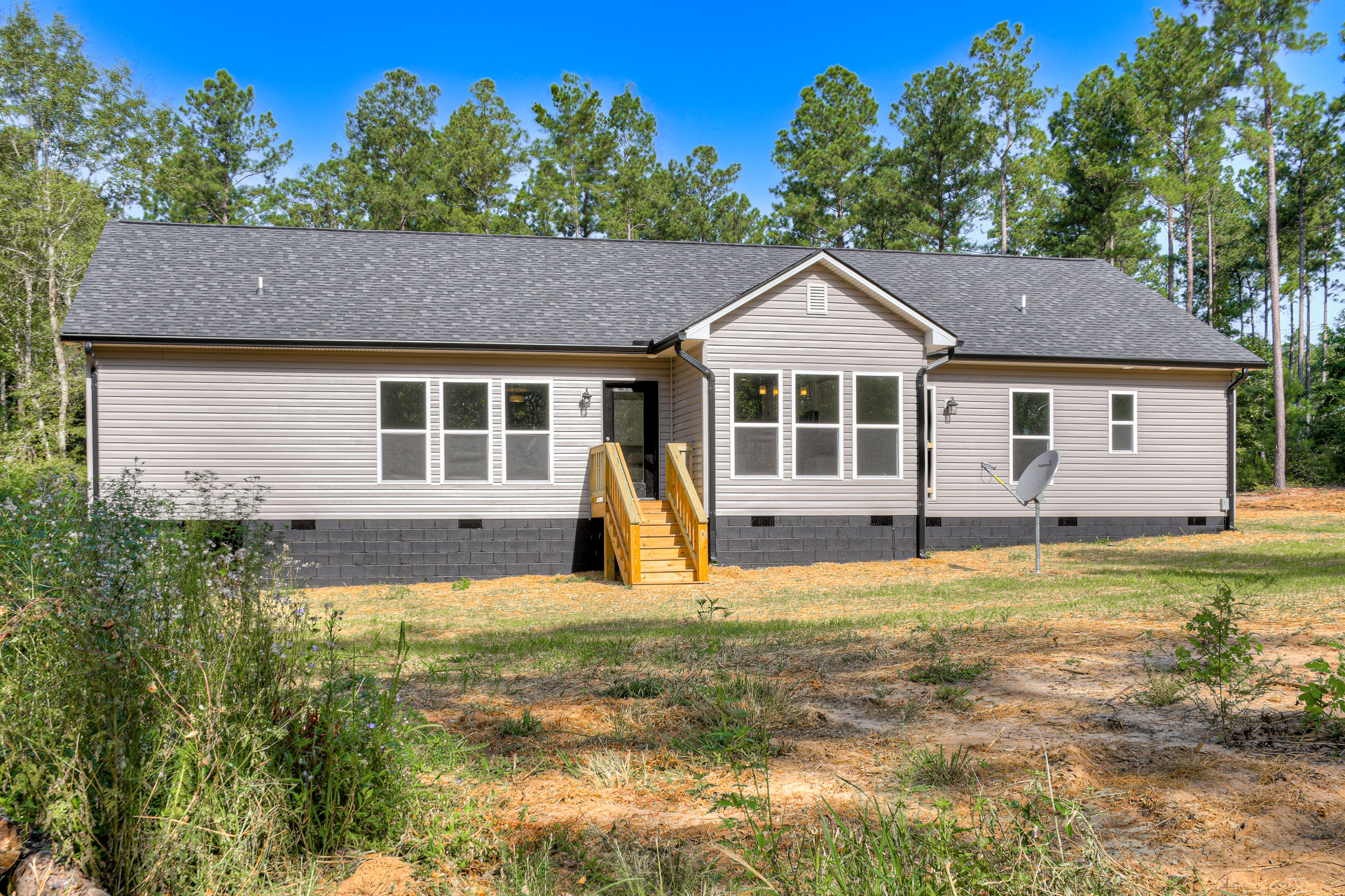 Two-story cottage with wooden exterior staircase, white-trimmed windows, yellow-lit window, satellite dish, surrounded by grass and trees