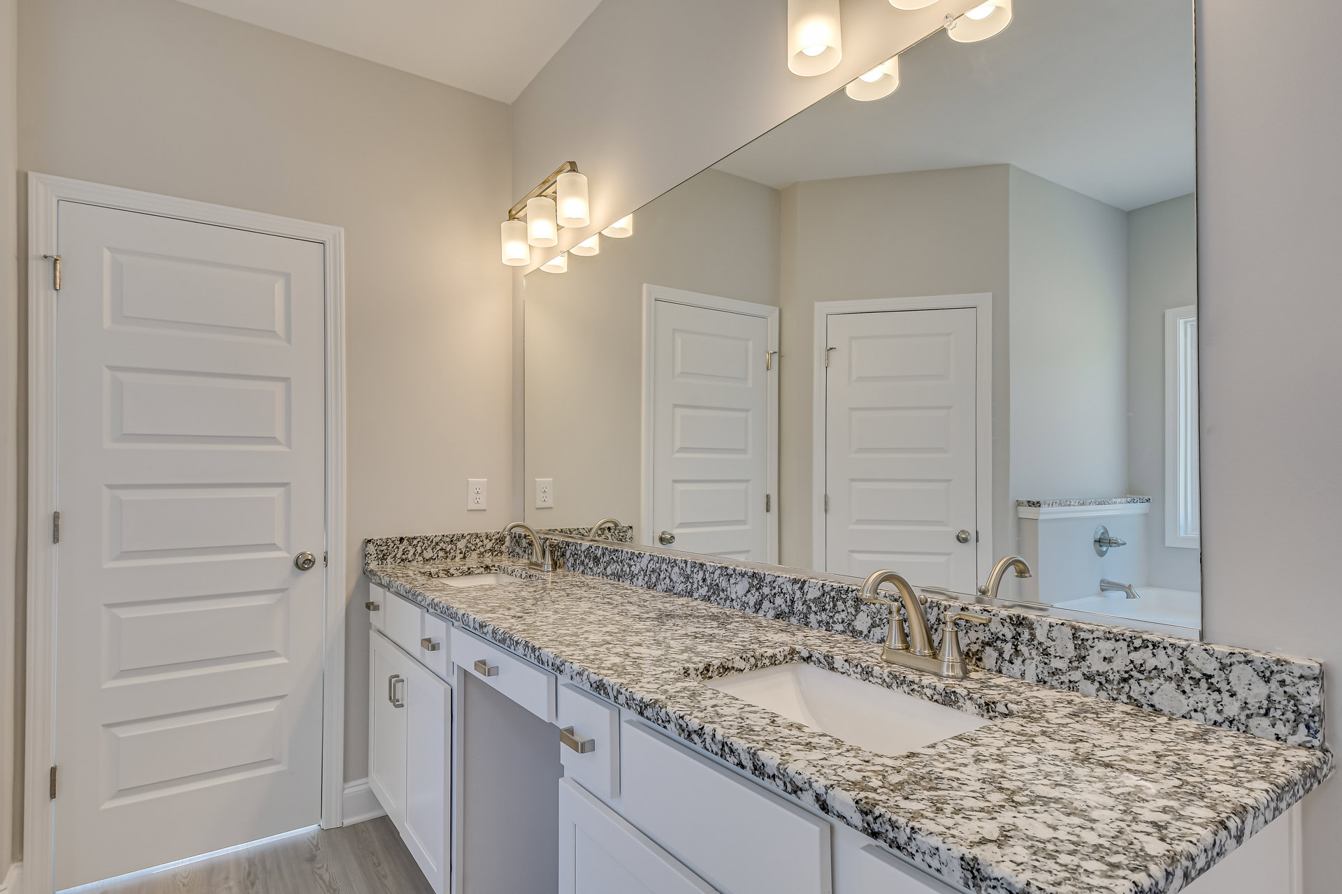 Bathroom with marble countertop, undermount sink, chrome faucet, large wall mirror, white cabinetry, and white door with silver handle