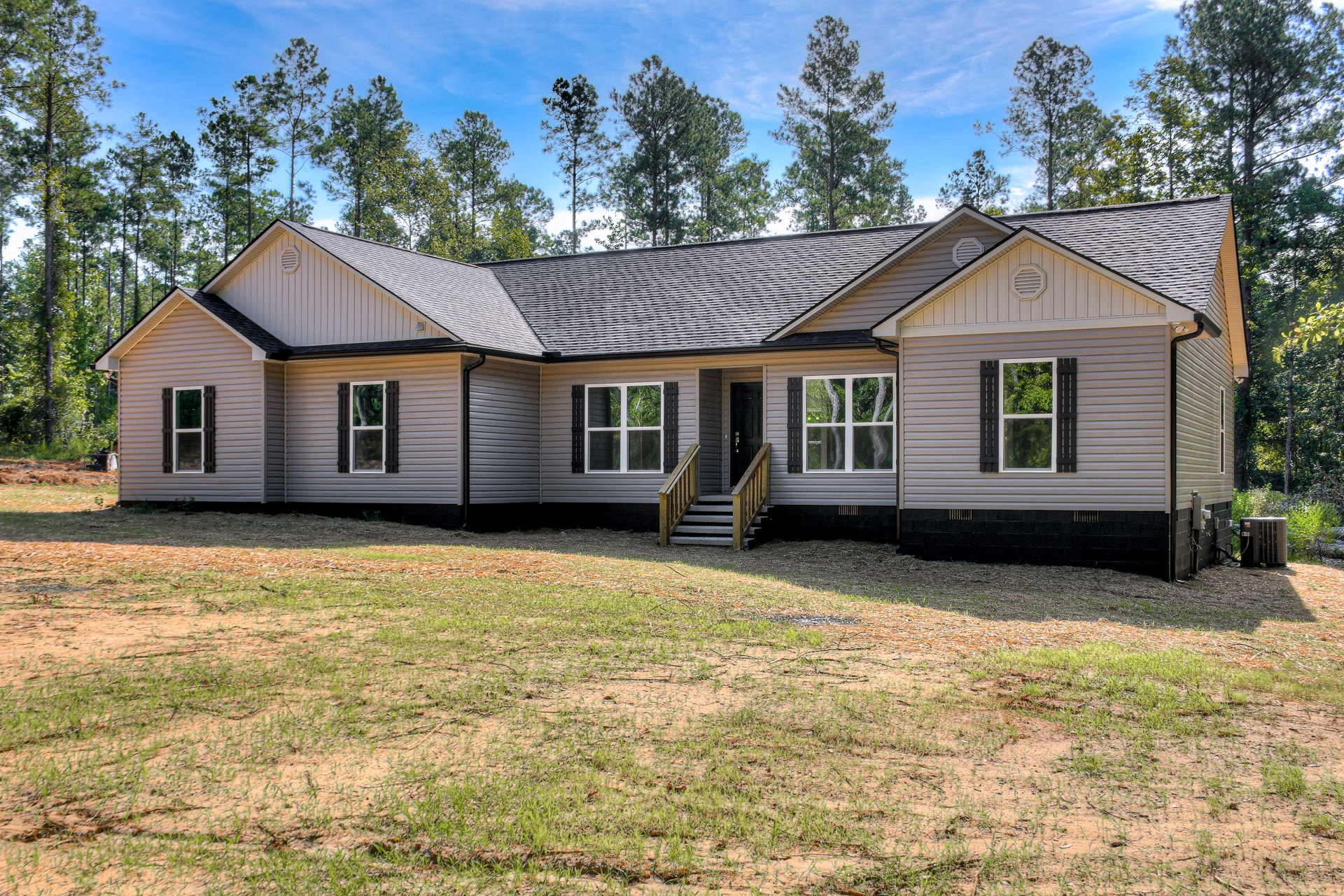 White-framed windows reflecting trees, wooden porch with stairs, grassy yard bordered by mature trees