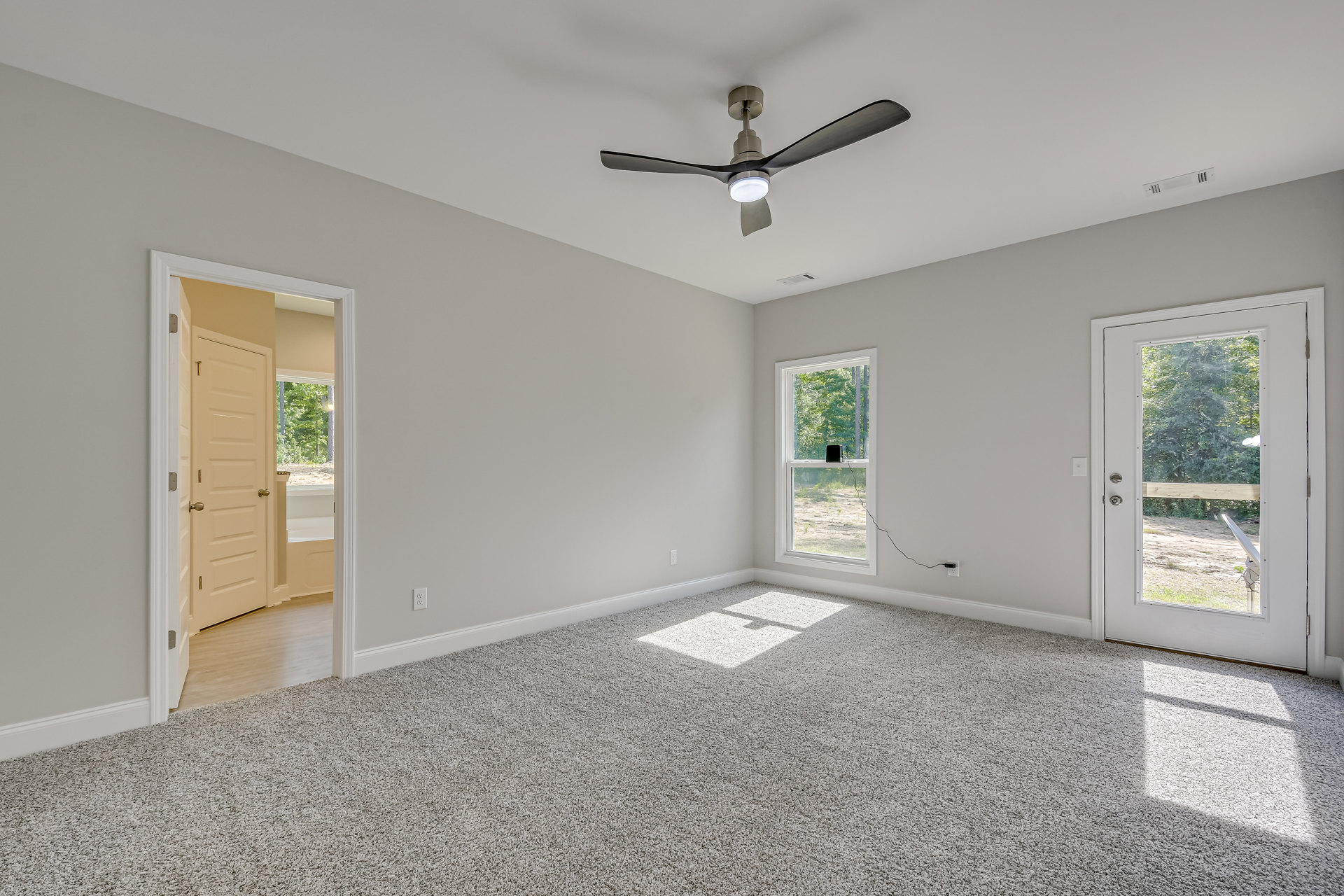Neutral-toned room with white carpet, ceiling fan with light fixture, large window, white-framed door, and smooth plaster walls