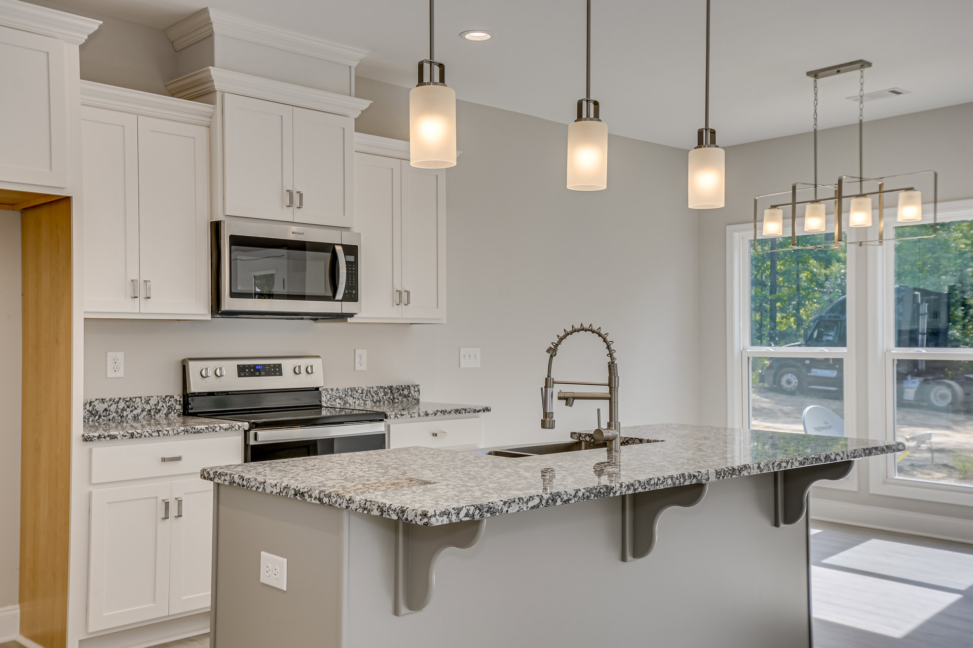 Granite countertop kitchen with stainless steel microwave, undermount sink and chrome faucet, white cabinetry, and modern pendant light fixture