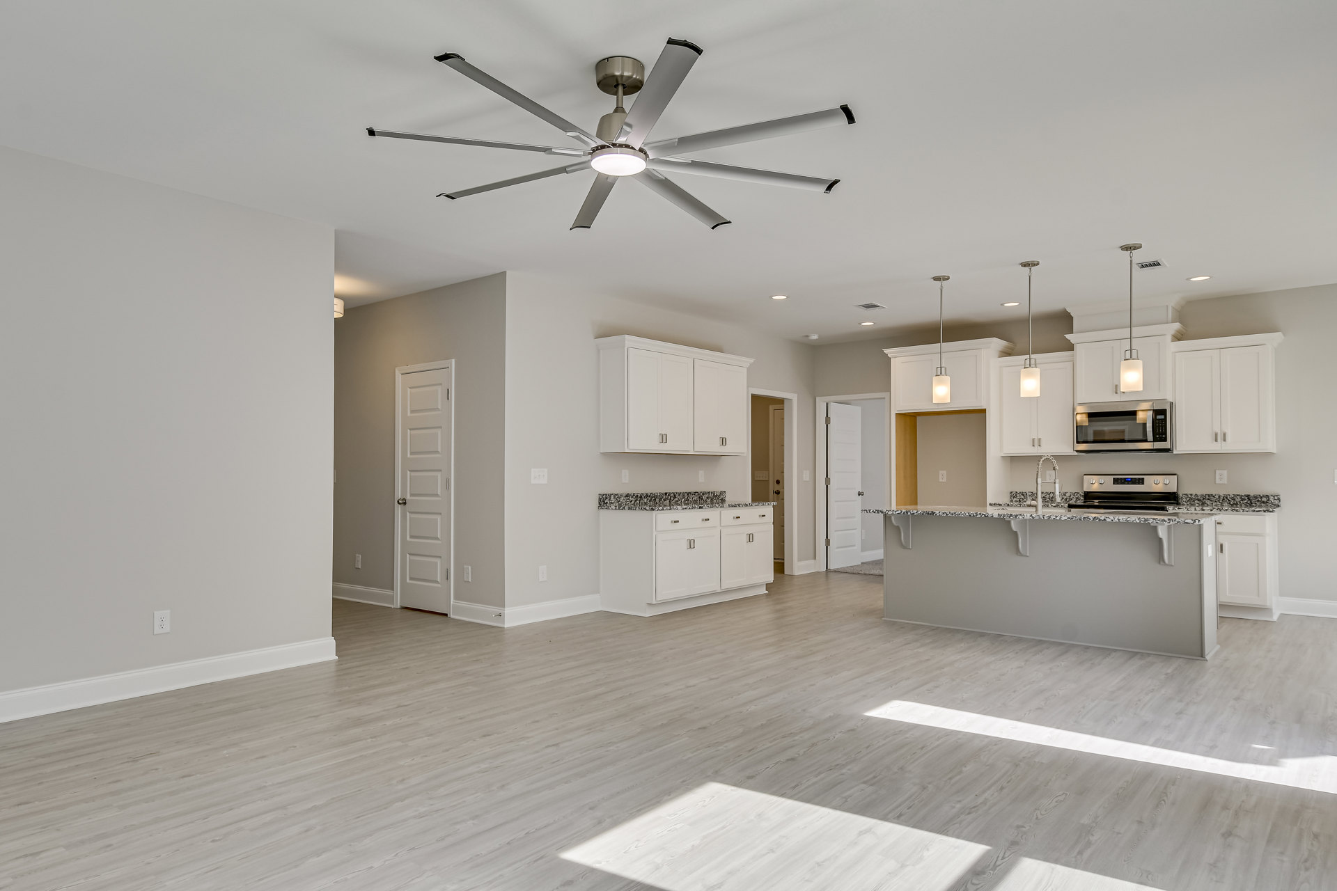 Open-concept kitchen with white cabinetry, stainless steel appliances including an open microwave, light wood flooring, a central island with dual sinks, and a ceiling fan with
