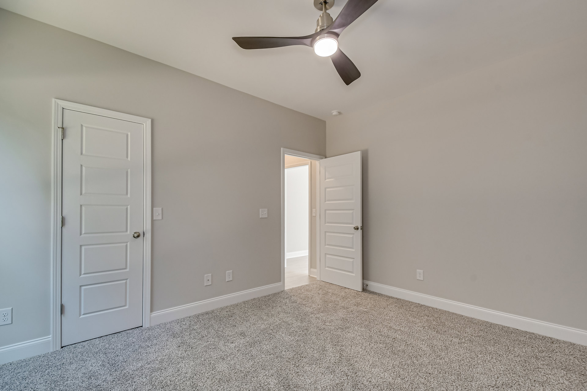 Ceiling fan with integrated light fixture mounted on white ceiling above carpeted floor, white door with silver knob and light switch visible on wall