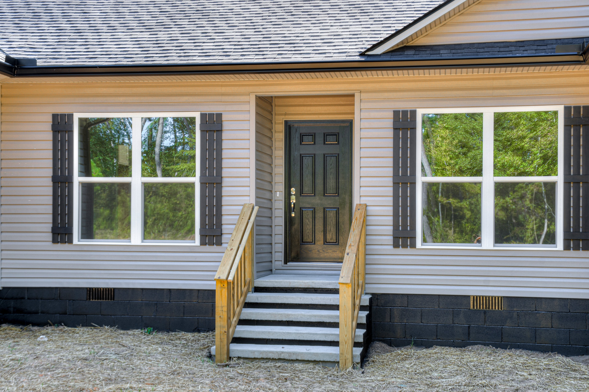Wooden front stairs with black door, white siding, porch, and large window reflecting trees