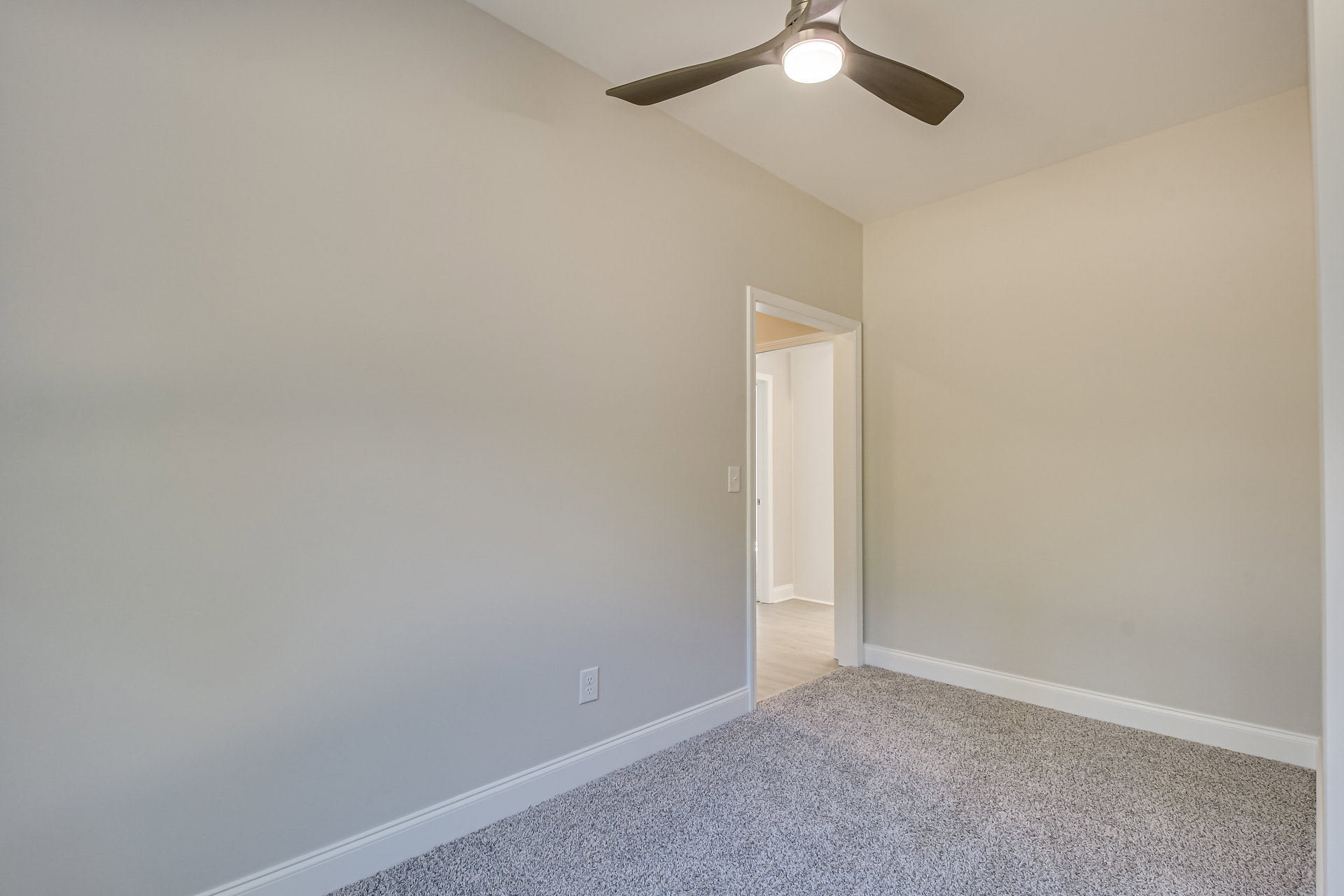 Ceiling fan with integrated light fixture mounted on white ceiling, white walls, black and white speckled carpet flooring, white door visible in corner