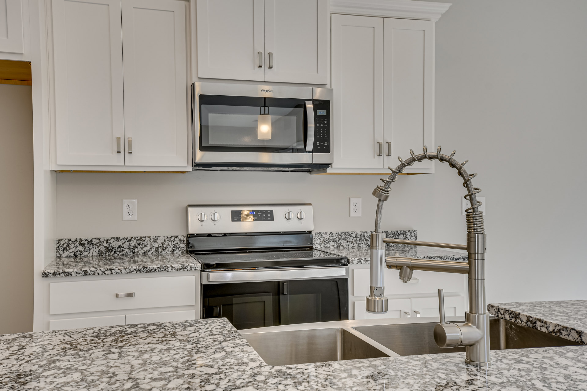 White kitchen with stainless steel sink, chrome faucet, built-in microwave with illuminated interior, digital stove, white cabinetry, and light stone countertop