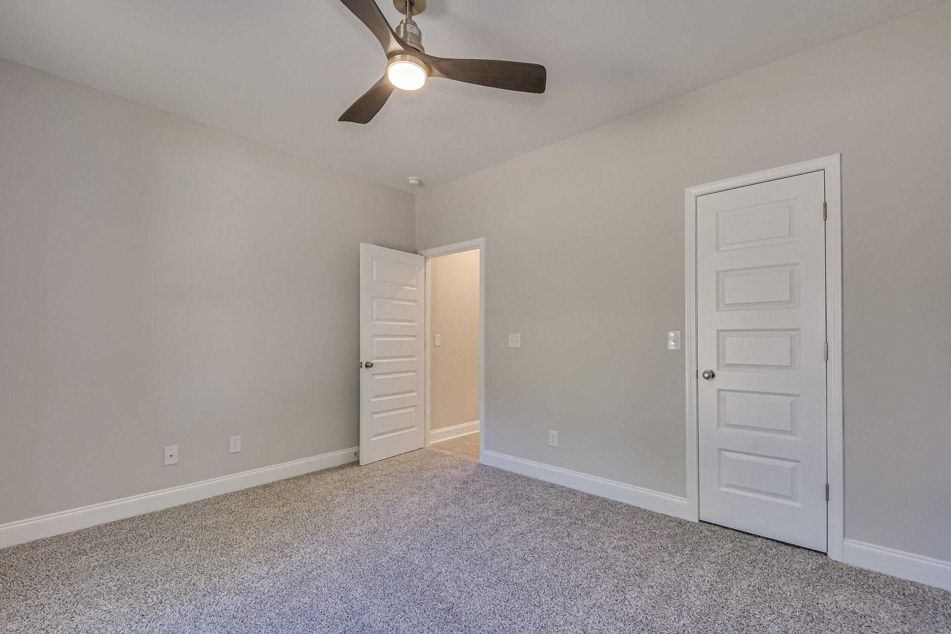 Carpeted room with white walls, ceiling fan with light fixture, and white door featuring a silver handle