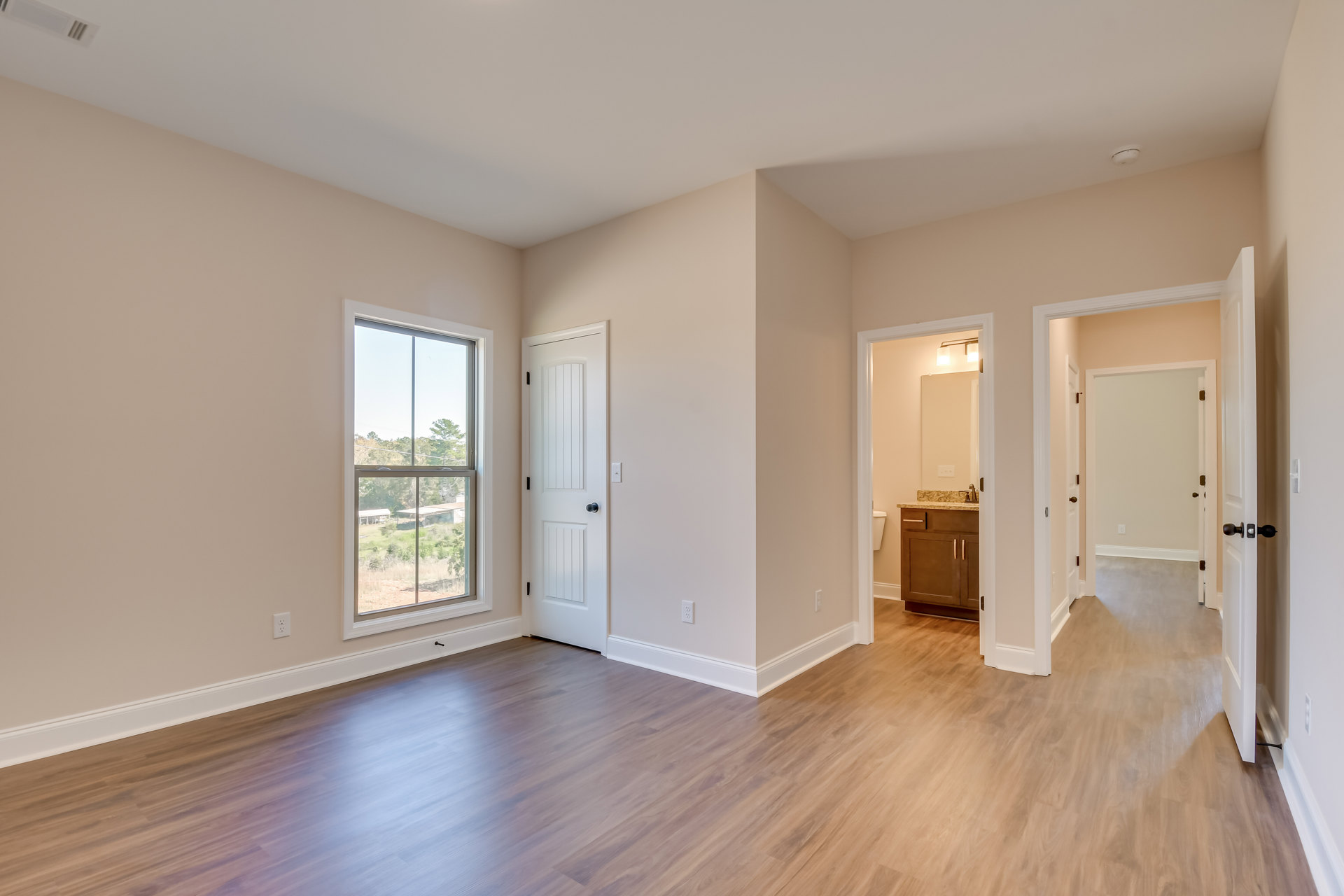 Wood flooring and white walls in a bright room with a large window overlooking trees, white door with black knob, and a close-up of a cabinet.