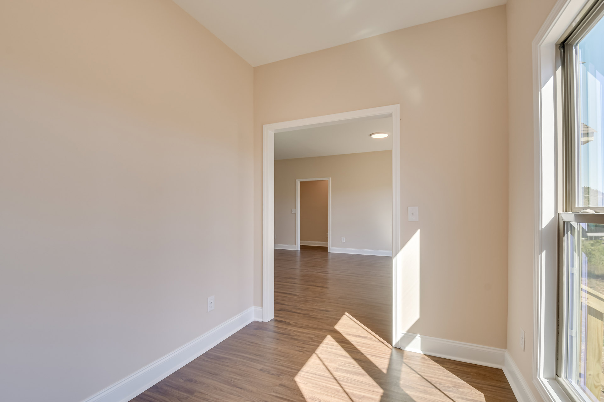Open white-trimmed door in room with brown walls, wood flooring, and window with white frame