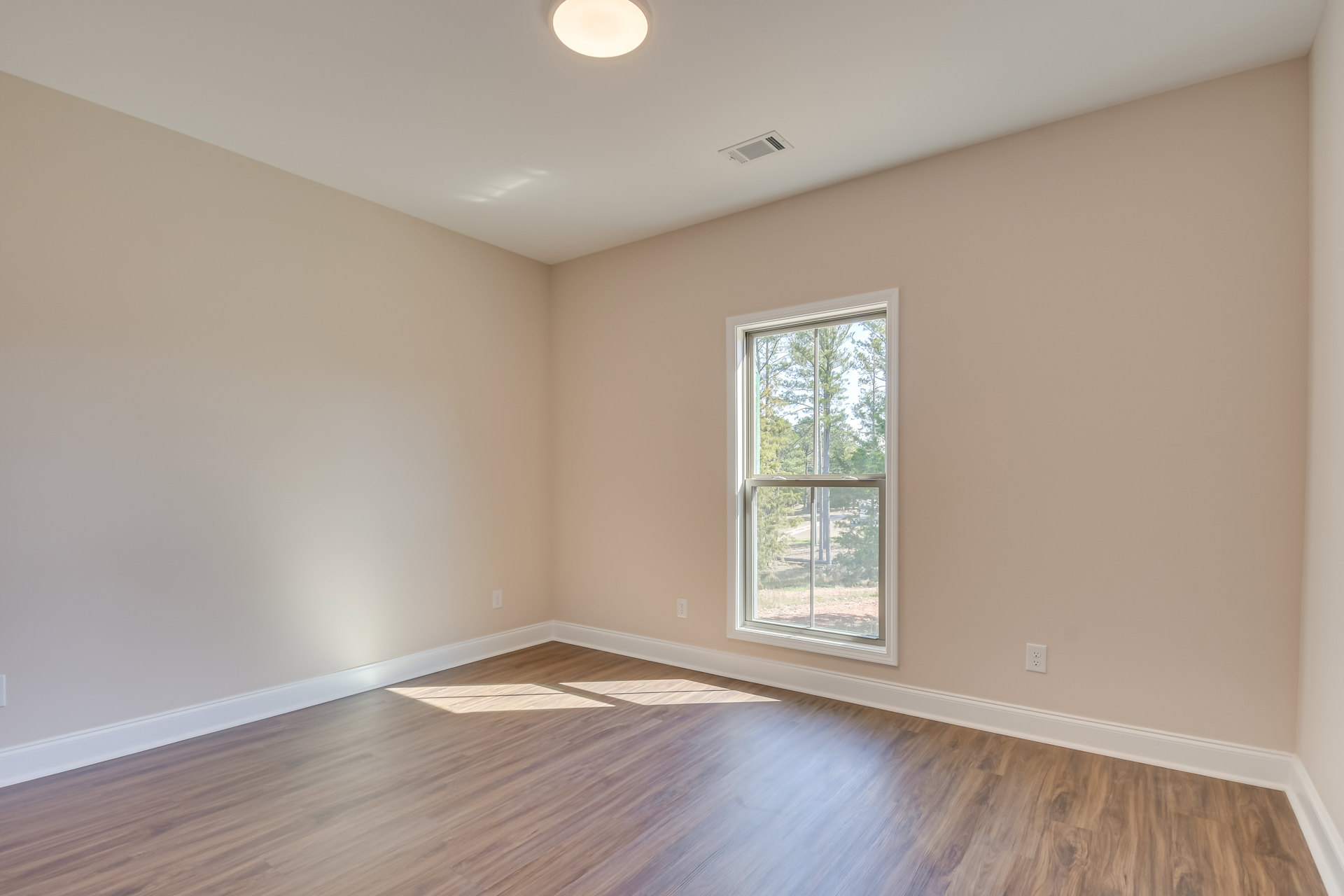 Hardwood floor with white baseboard trim, large window overlooking trees, plaster walls, ceiling vent, recessed light fixture