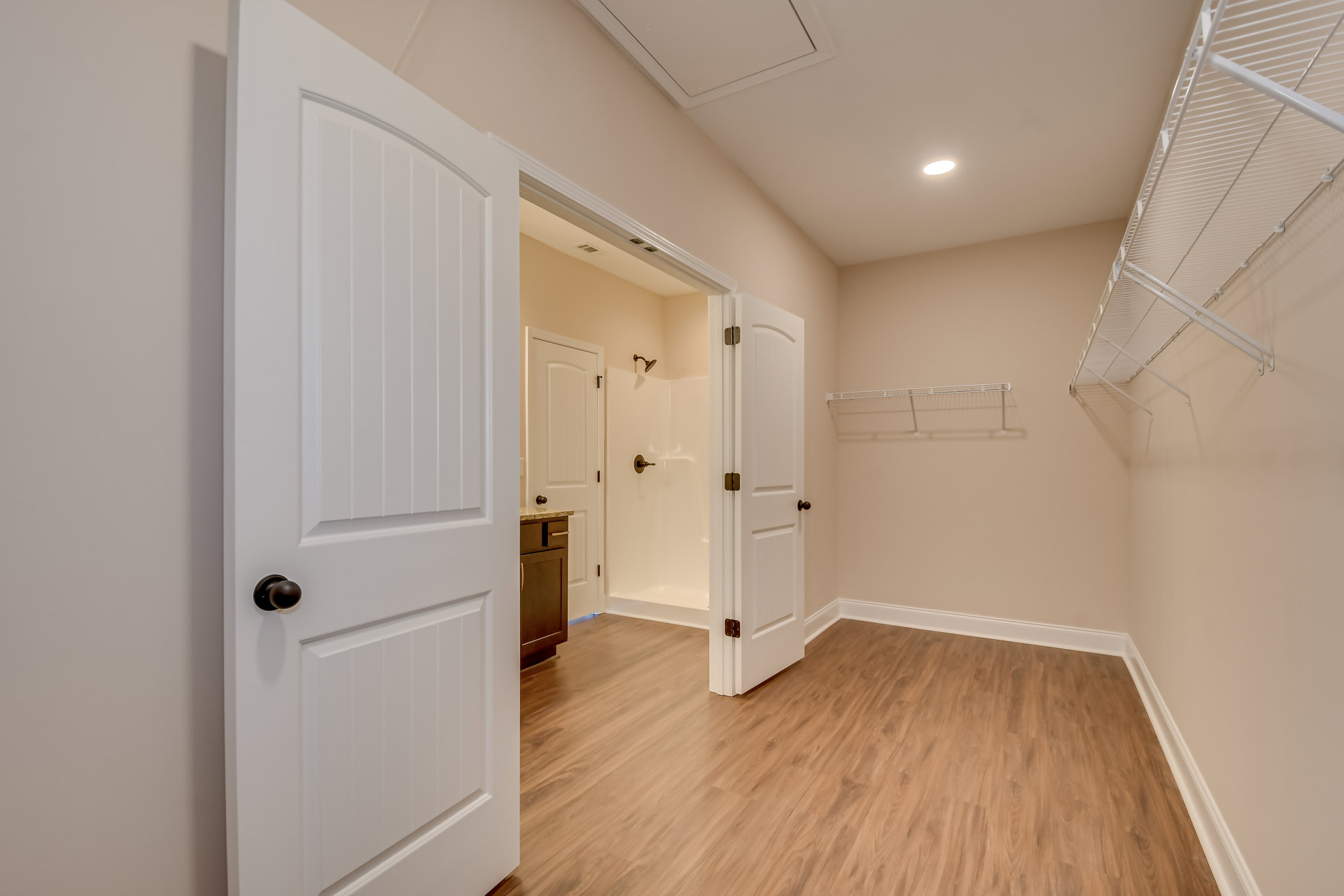 White paneled doors with black knobs, wood laminate flooring, brown cabinet with metal handle, white shelving with metal rods, plaster walls