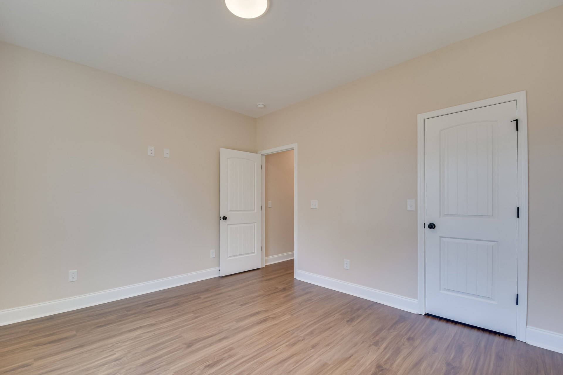 Hardwood floor room with multiple white doors featuring black knobs, white walls, recessed ceiling light, and square panel door design