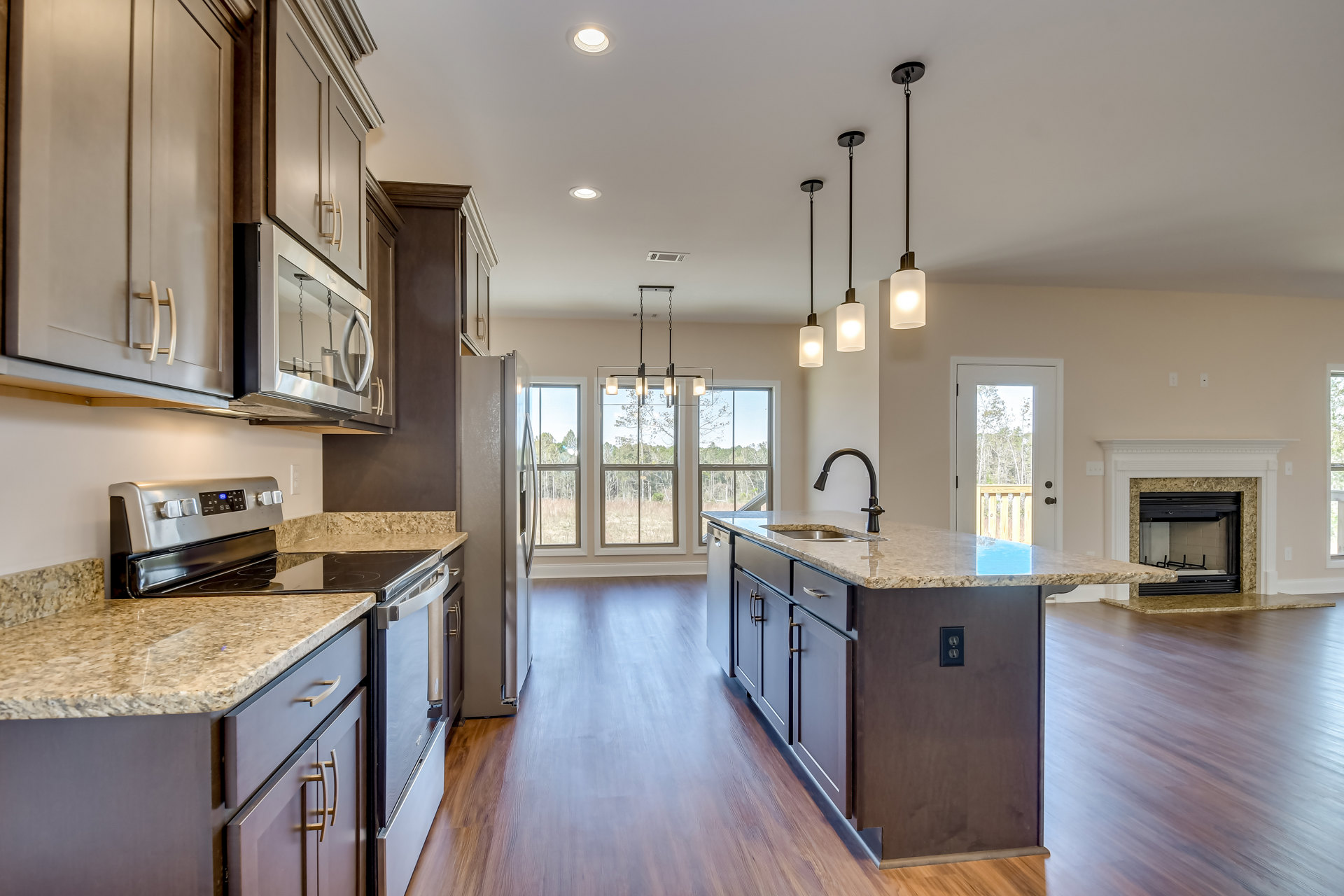 Spacious kitchen featuring a large central island with granite countertops, stainless steel refrigerator, white cabinetry, and wood flooring