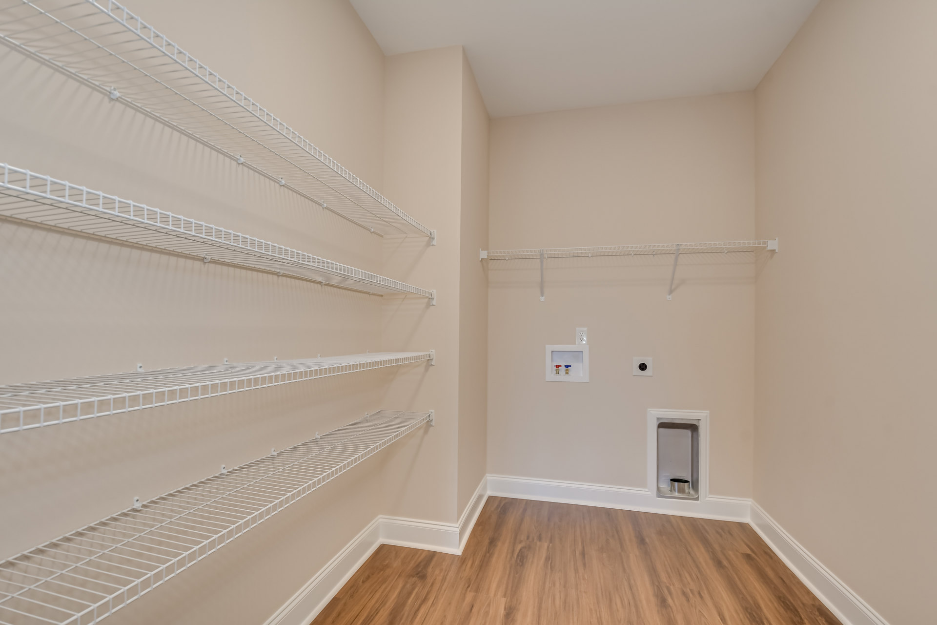 Empty closet with white wire shelving, wood floor with white trim, white wall featuring a small silver cup and a white box with two valves