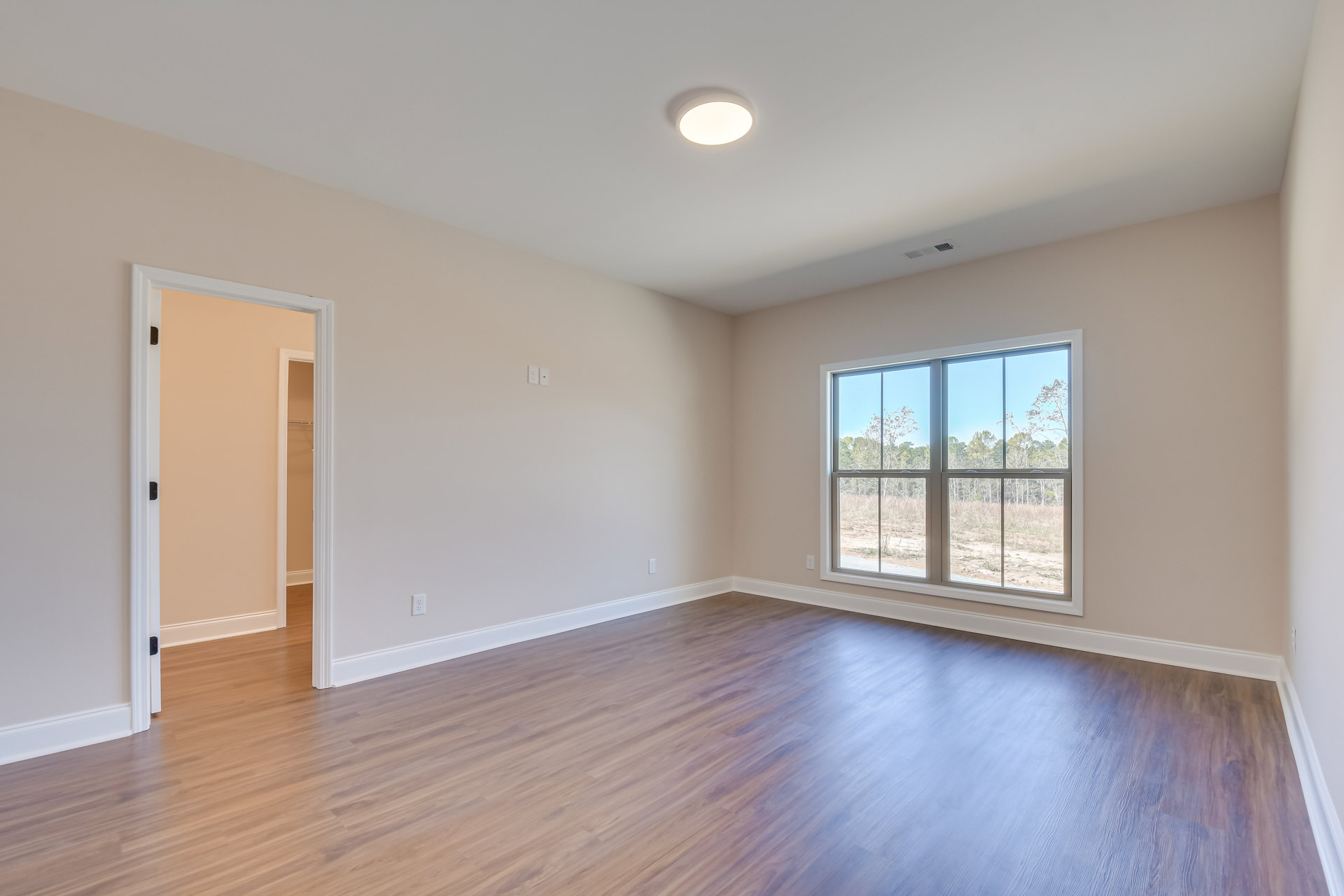 Wood flooring in a bright room with a large window overlooking trees, ceiling light fixture, and open door revealing closet space