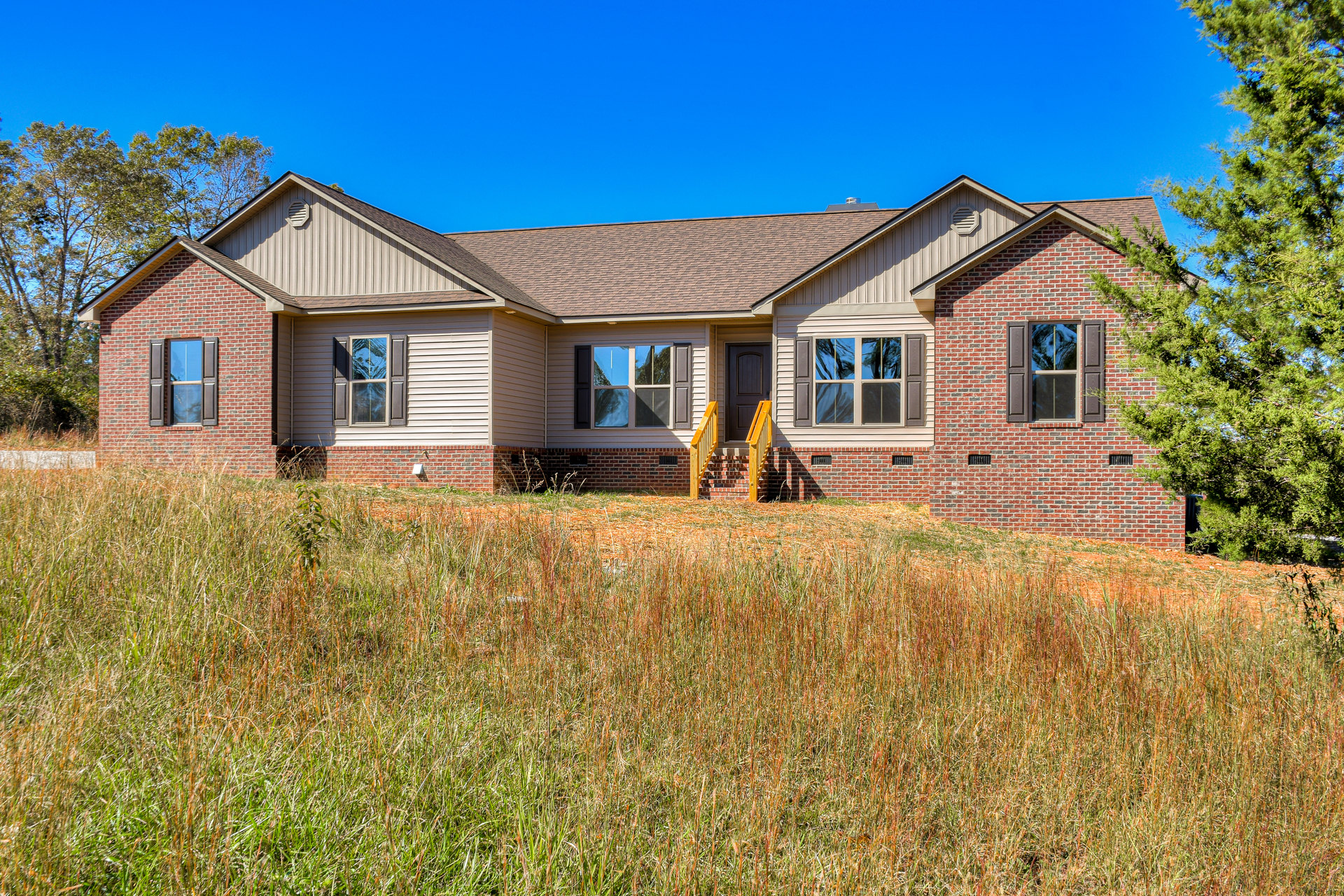 White cottage-style home with large windows reflecting trees, front porch with stairs, surrounded by a lush grassy lawn and mature trees under a clear sky