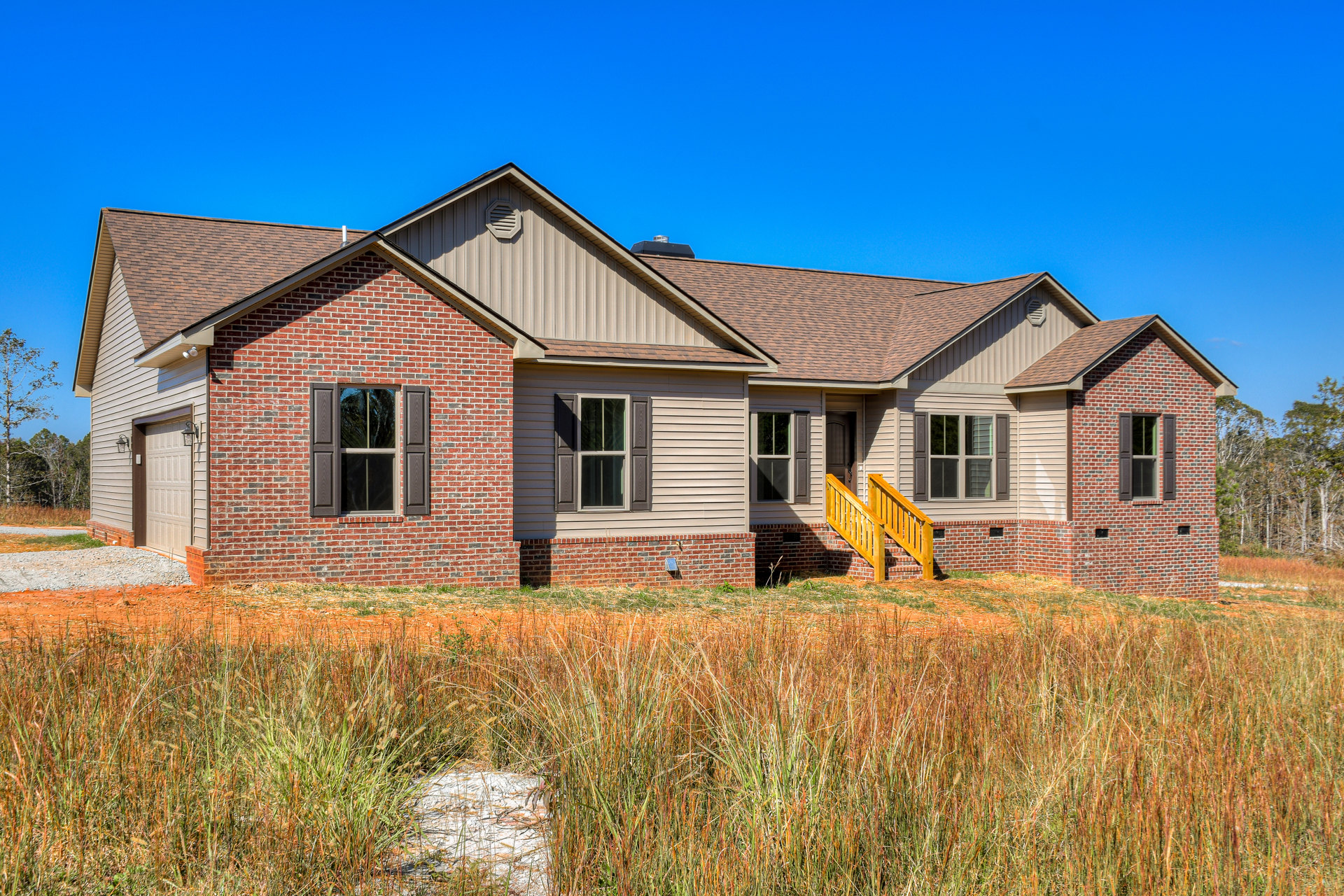 Brick house with white-framed windows, wooden railings on a brick staircase, grassy lawn in front, tree reflections visible in window glass