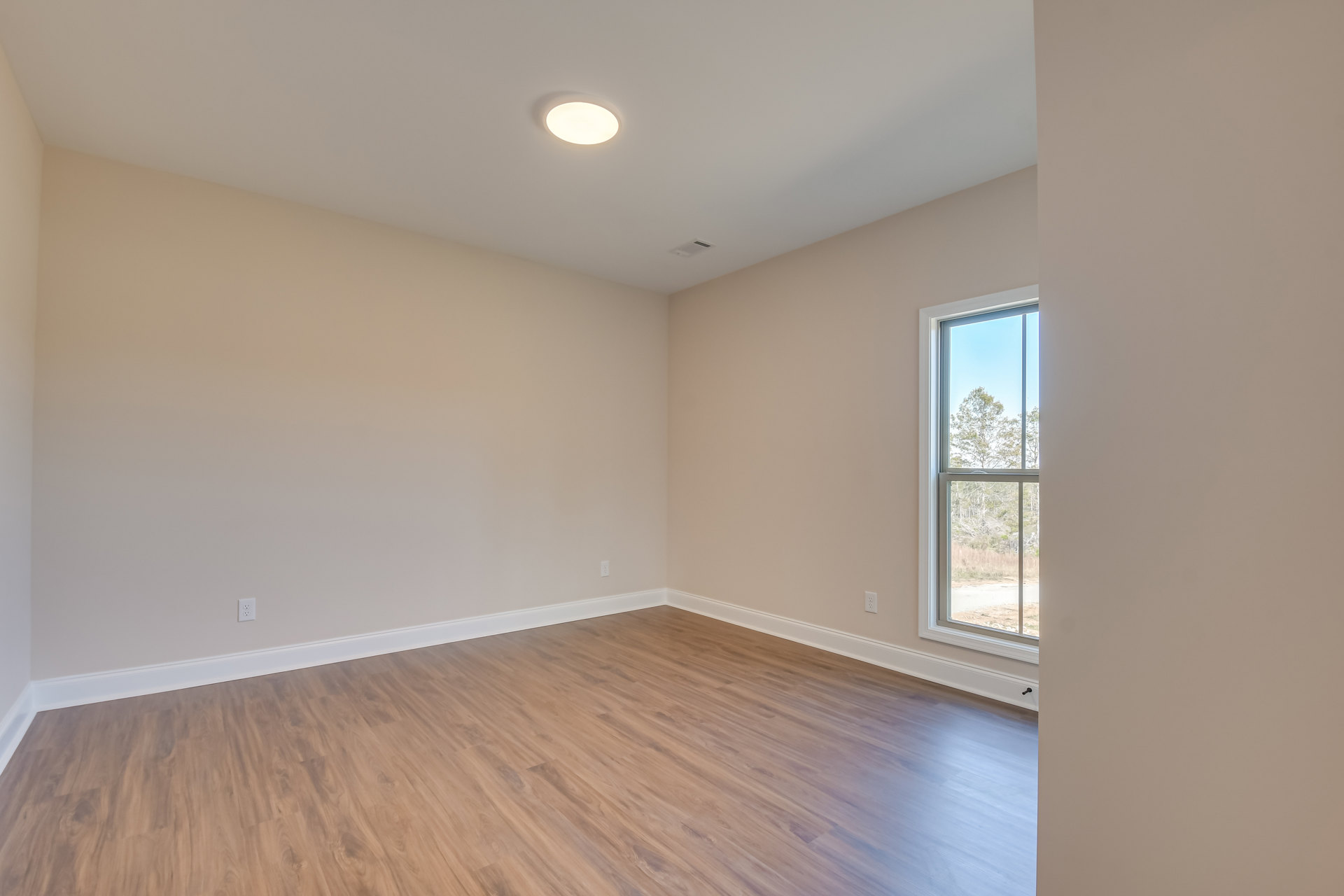 Wood flooring in a bright room with plaster walls, large window overlooking trees, and modern light fixture