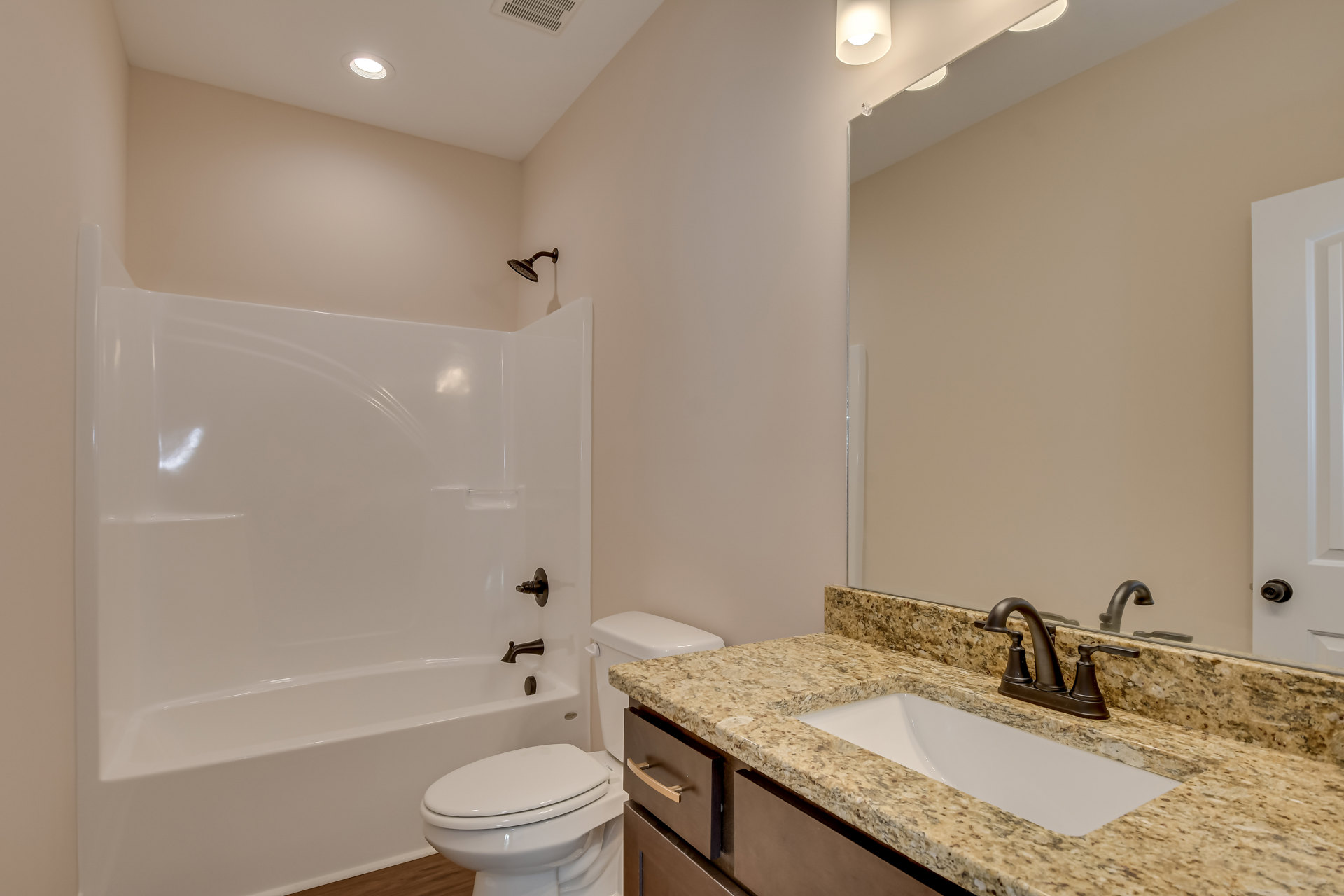 White bathtub, toilet with closed lid, wall-mounted sink with chrome faucet, rectangular mirror above sink, light-colored tile walls, curved shower head, neutral finishes