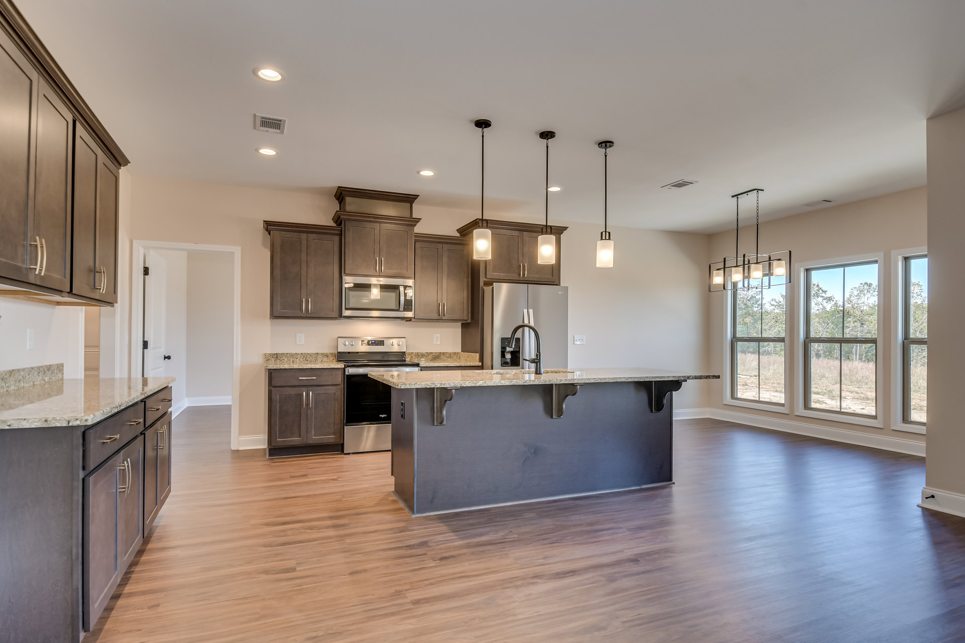 Spacious kitchen featuring a large central island with white countertop, wood flooring, stainless steel appliances including stove and microwave, white cabinetry, undermount sink