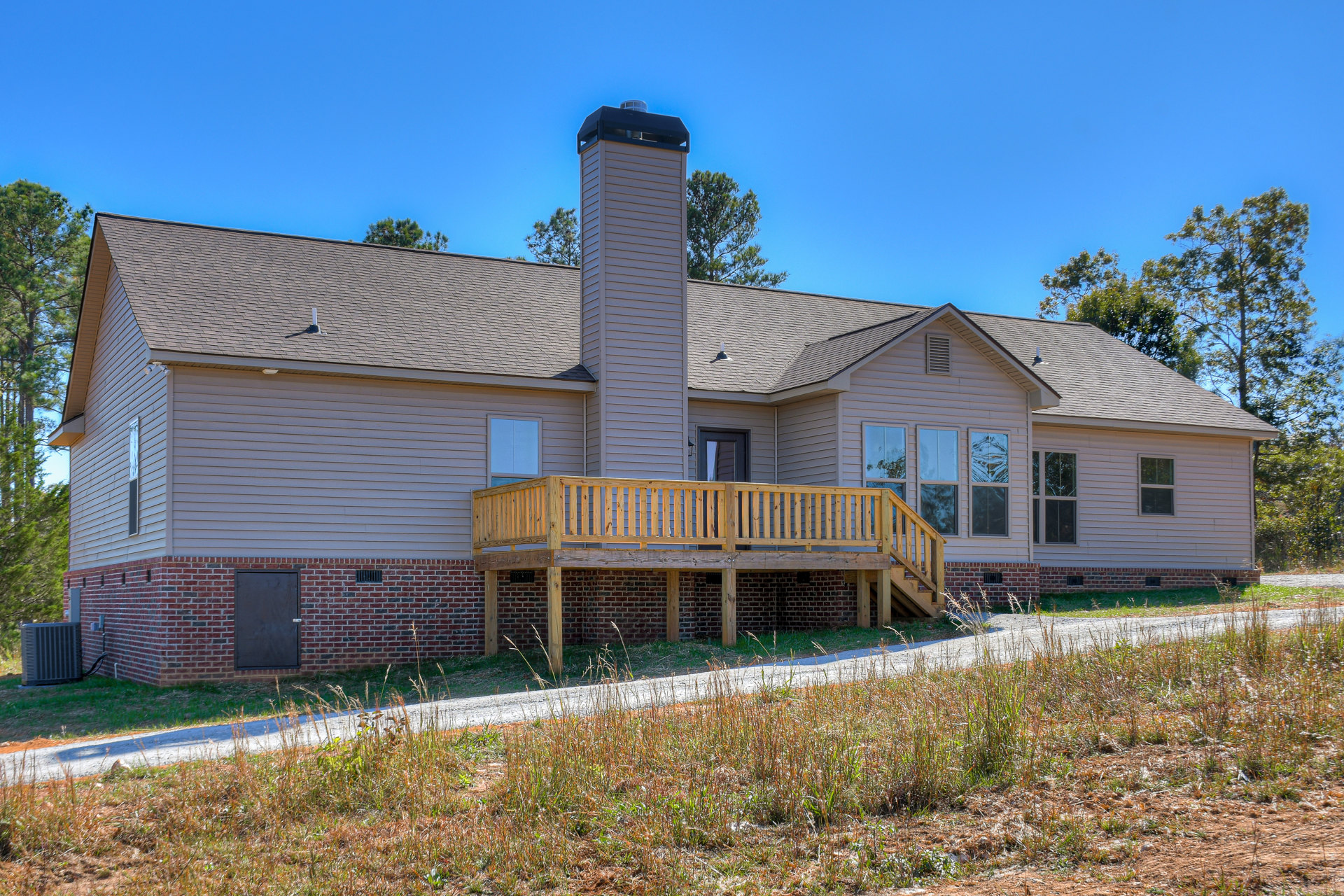 Two-story house with brick chimney, covered porch, wooden deck, white siding, and grassy lawn