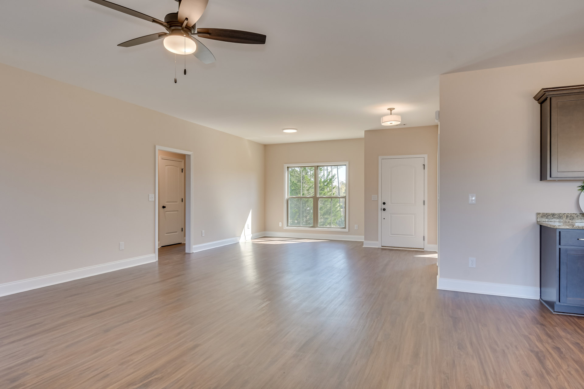 Wood flooring, white walls, ceiling fan with light, white door featuring black handle, window overlooking trees