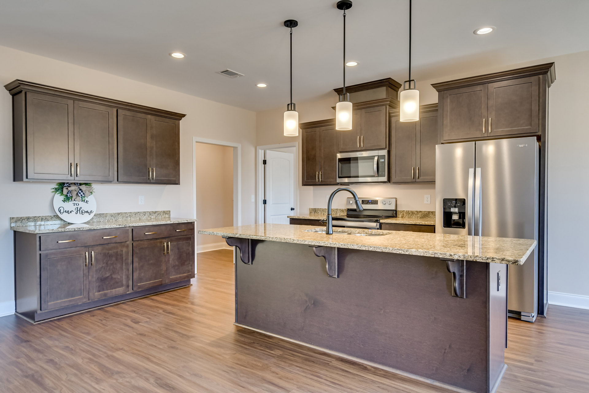 Spacious kitchen featuring a large marble-topped island, stainless steel refrigerator, white cabinetry, built-in microwave, and wall-mounted light fixture