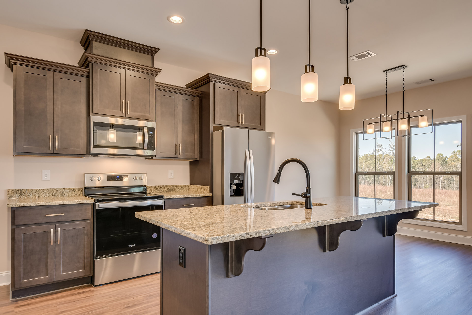 Spacious kitchen featuring a large central island with stone countertop, stainless steel refrigerator, stove with matching range hood, built-in microwave, modern sink and faucet