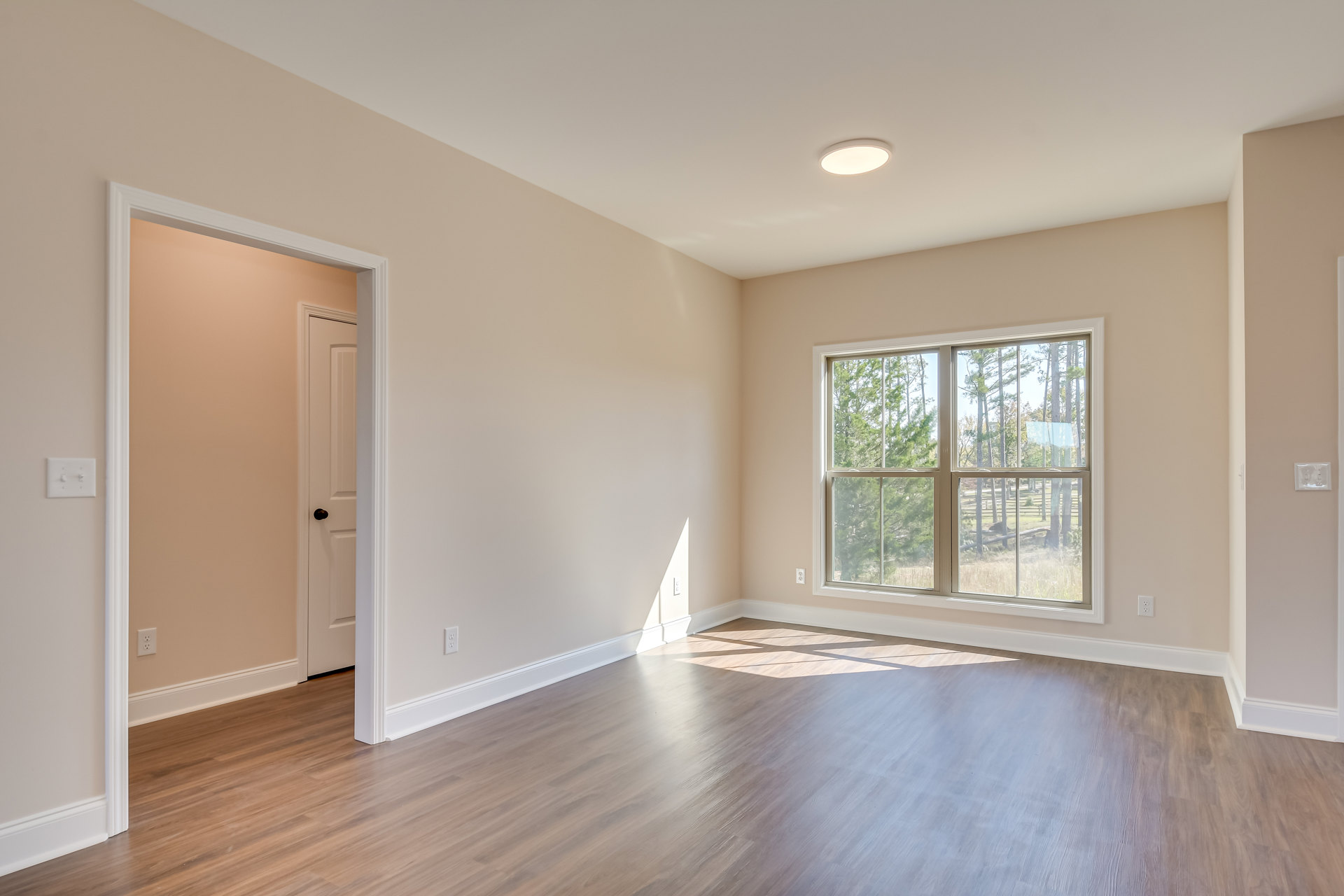 Hardwood floor room with white trim, large window overlooking trees, neutral walls, ceiling light fixture, door visible