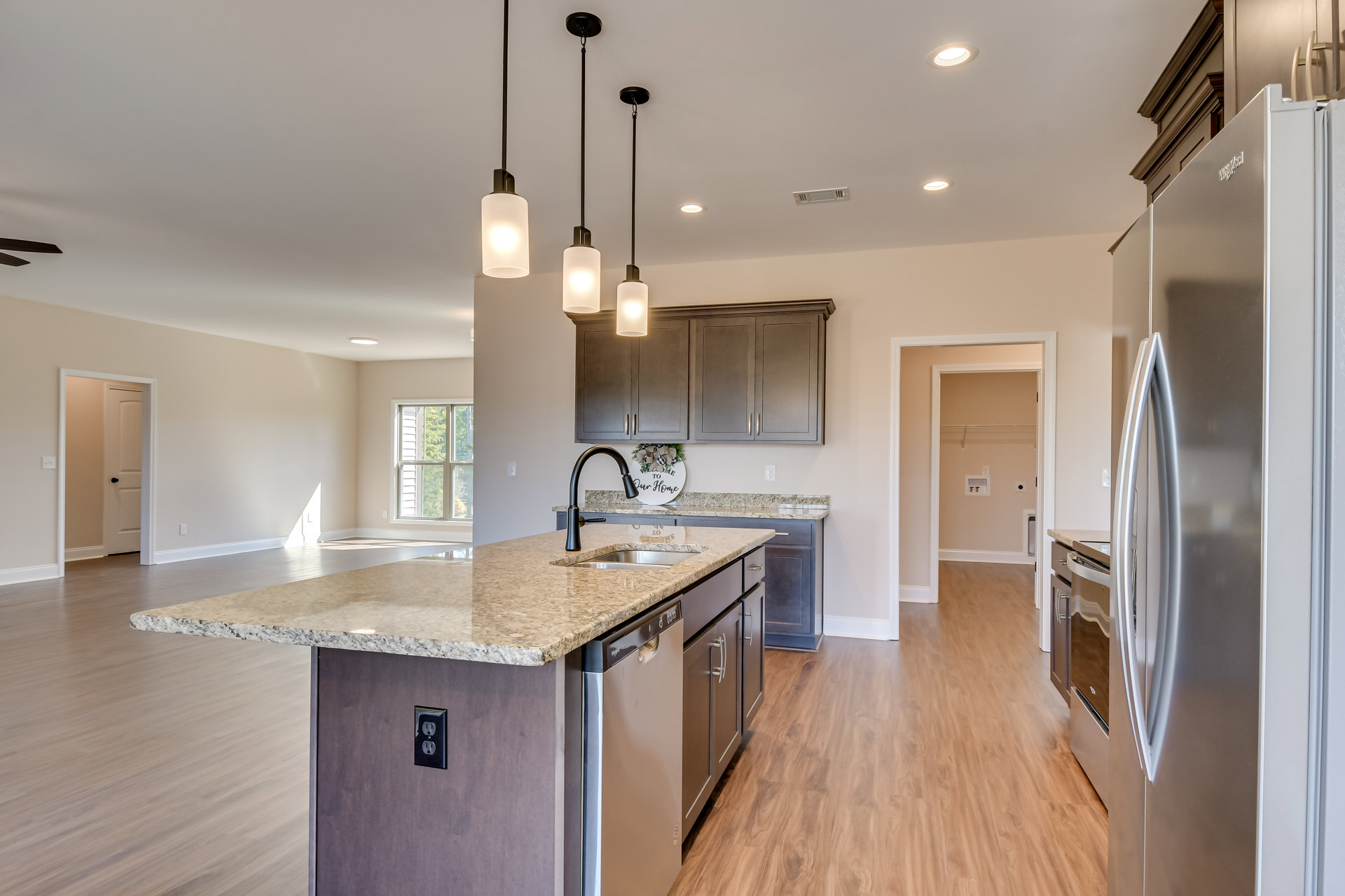 Granite kitchen island with undermount sink, wood flooring, white cabinetry, pendant light fixtures, recessed ceiling lights, and window with white trim