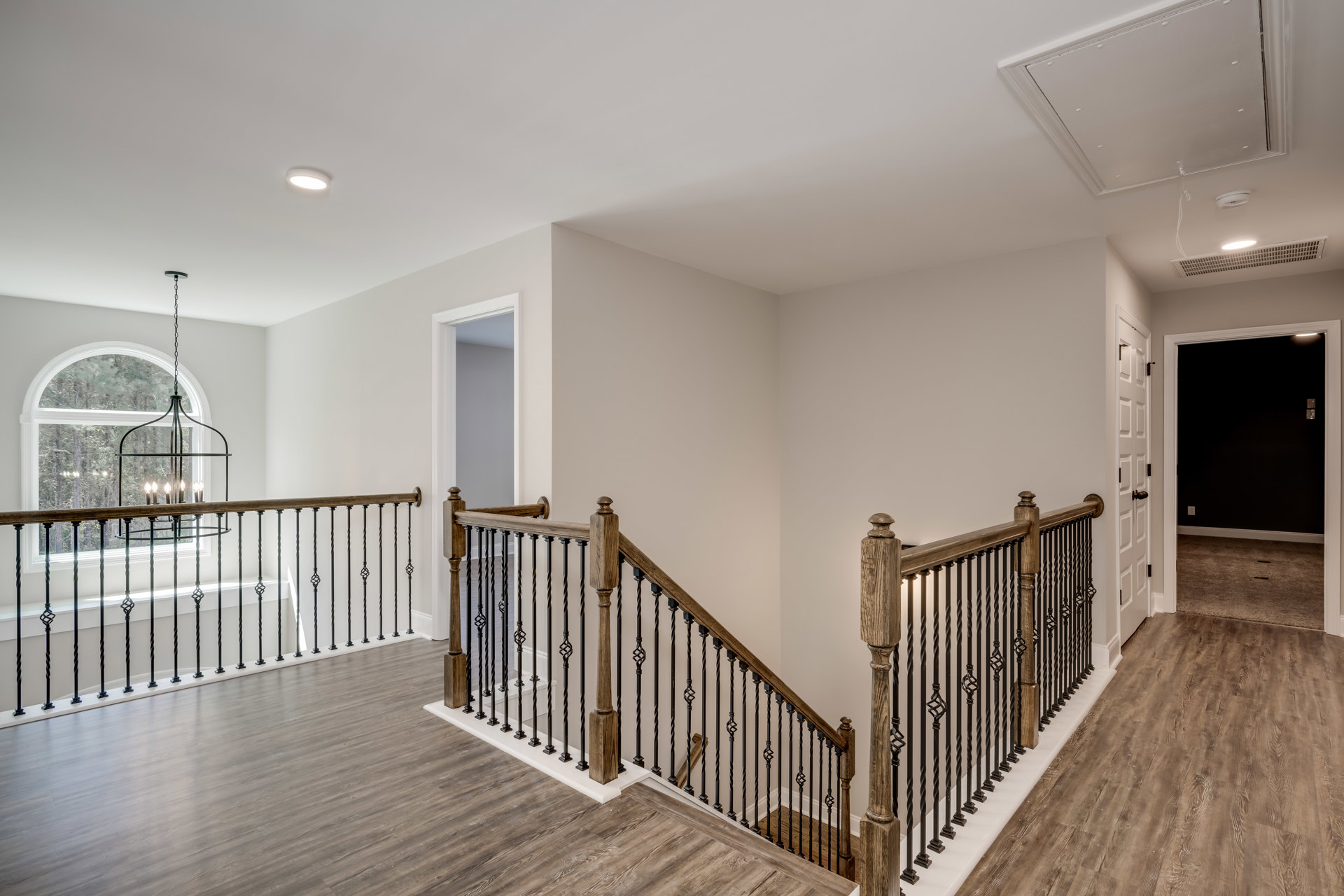 Wood staircase with matching railings and floor, black door with white frame, chandelier hanging above, white walls and ceiling.