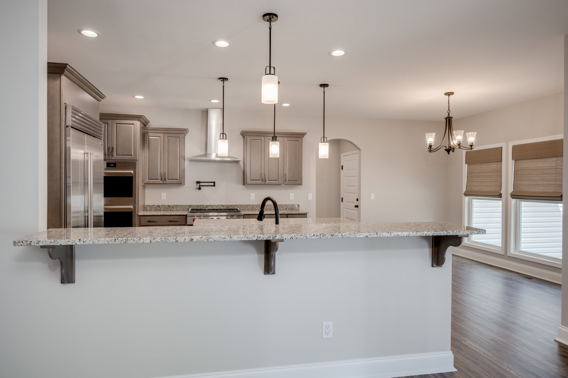 Open kitchen with wood flooring, bar seating, white cabinetry with metal handles, stone countertop featuring sink and stove, wall-mounted light fixture, recessed ceiling lighting