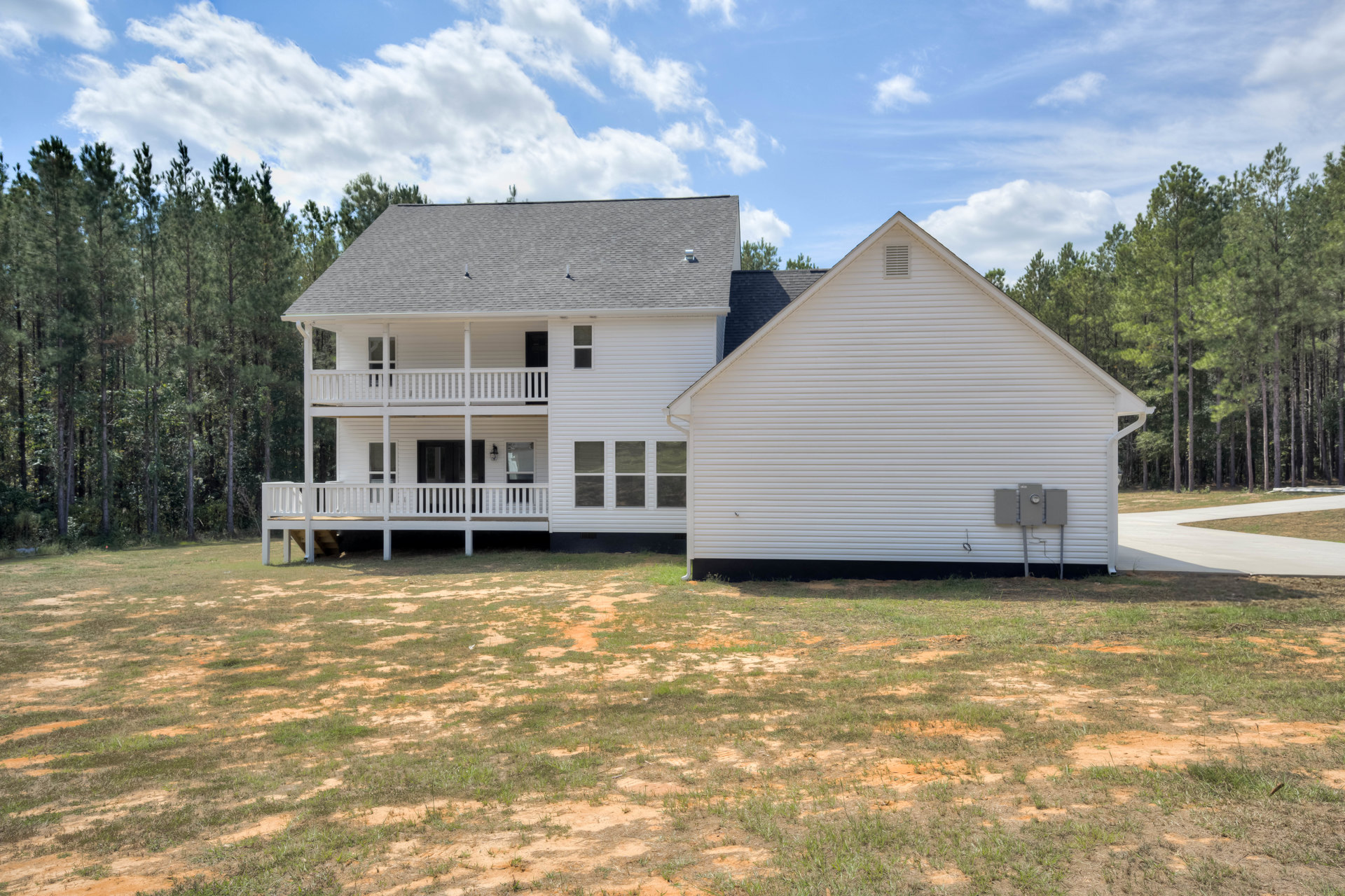 White house with spacious covered porch, white railings, grassy front yard, multiple windows, and chimney beneath a cloudy sky