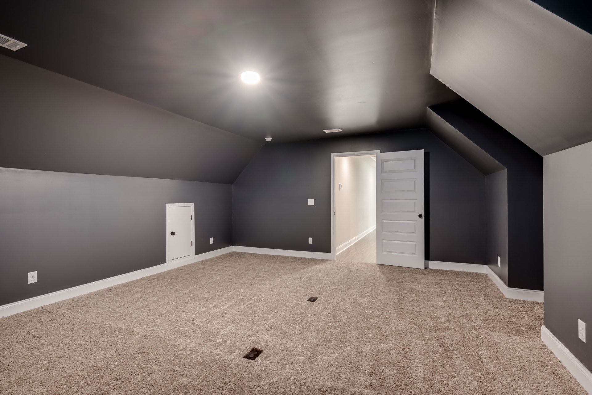 White carpeted room with white walls, white door featuring a black doorknob, electrical outlets, and light switch visible on the wall.
