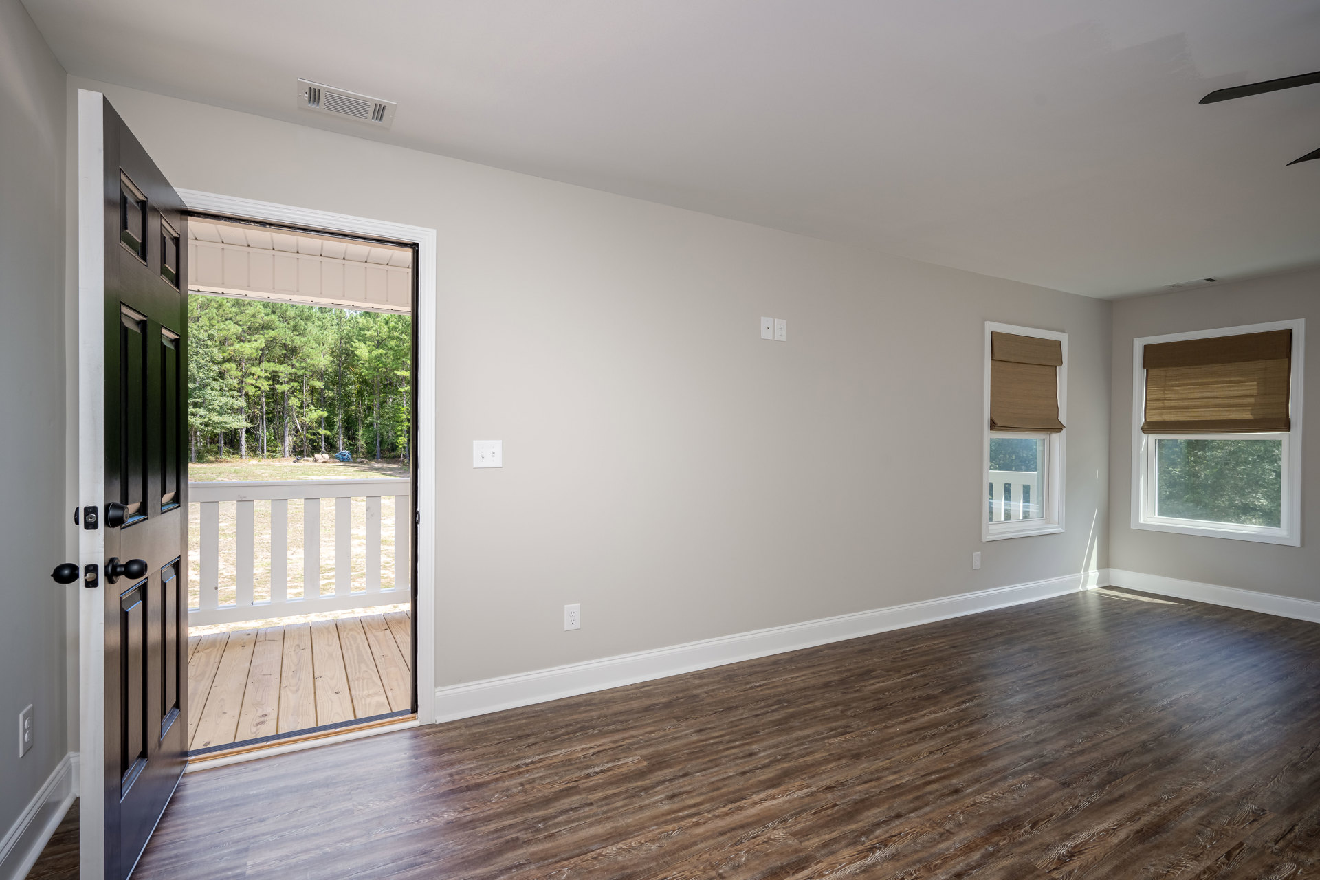 Wood floor room with white walls, electrical outlets, open door leading to outdoor deck, window featuring brown shade, door equipped with lock.