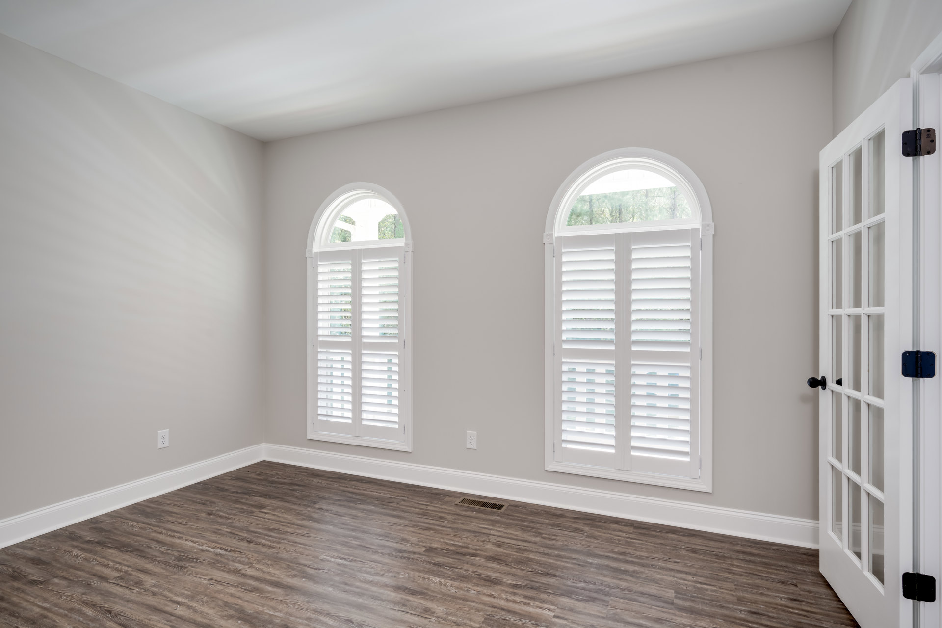 White walls with wide windows featuring white shutters and blinds, glass-paned door with black knob, wood laminate flooring, and decorative molding.