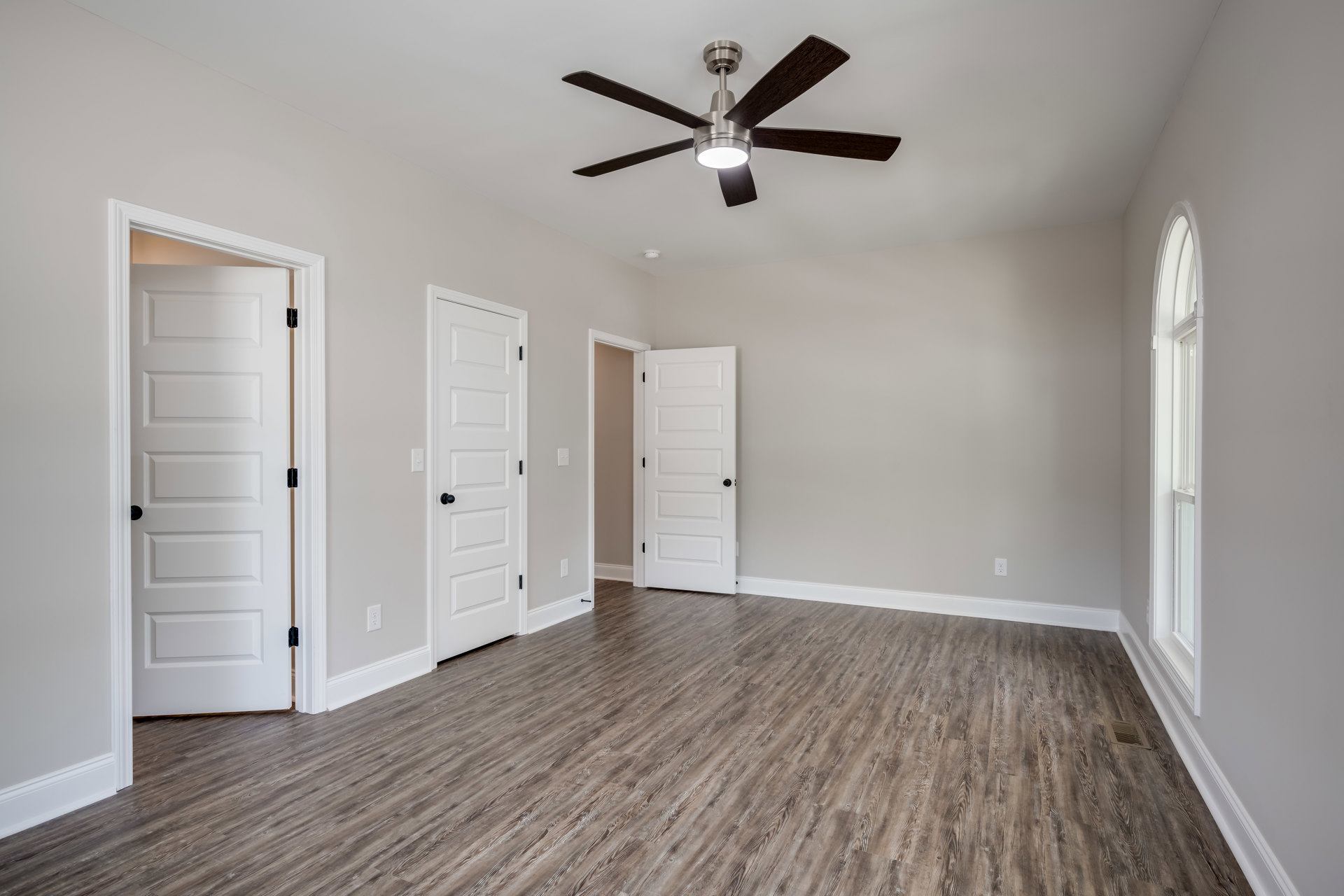 Wood flooring, white walls, ceiling fan with light, multiple white doors featuring black knobs and handles