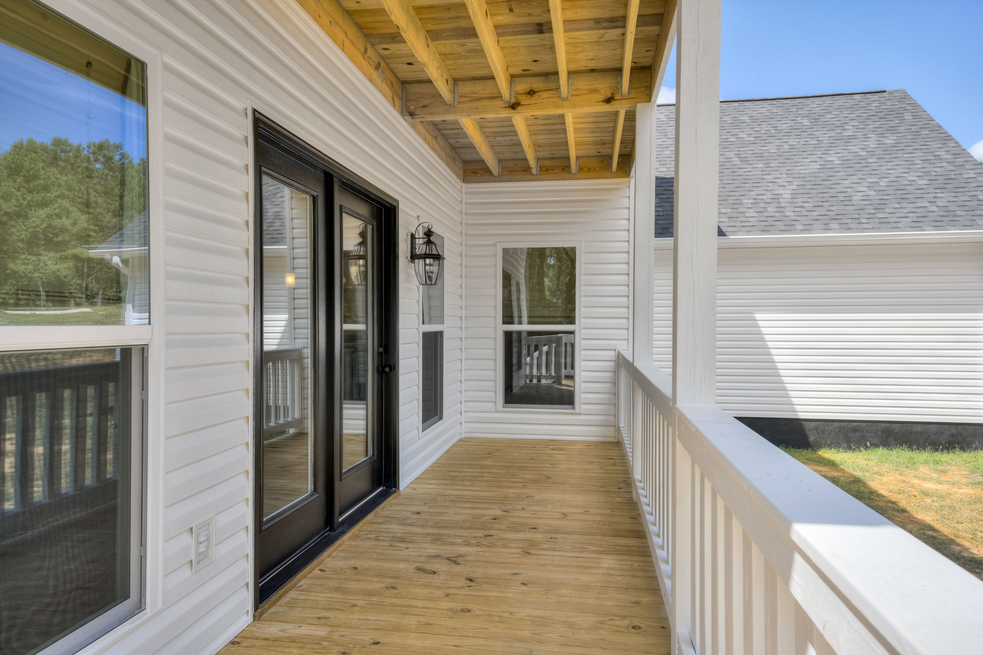 Wood deck porch featuring a black door with glass panels, white-framed window, screen door, and close-up of a modern light fixture against light siding